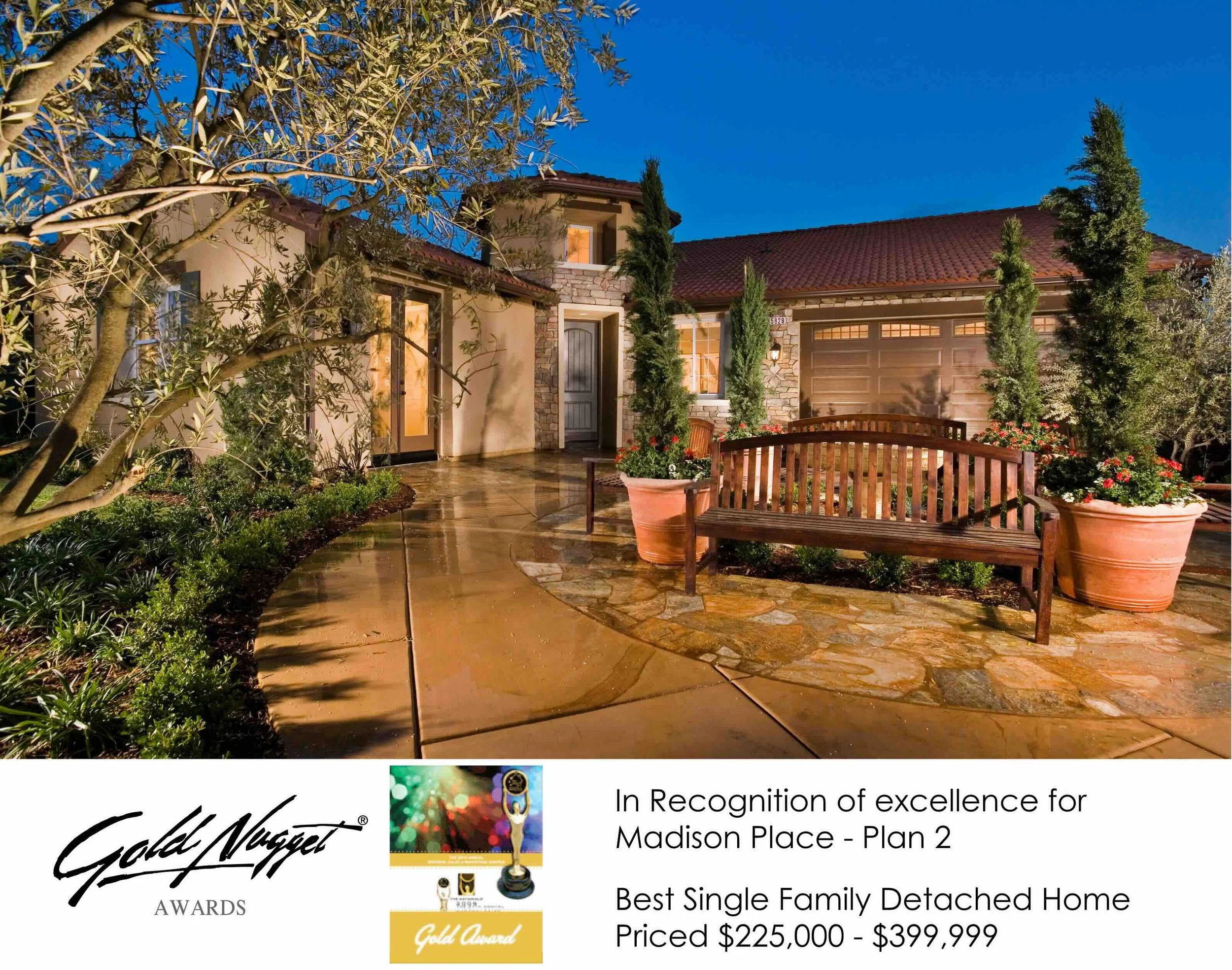The image shows the front of a beautifully lit single-family detached home with a curved wet stone and concrete walkway, potted plants, a wooden bench, and tall evergreen trees. The house has a stone and stucco exterior with a red tile roof, multiple