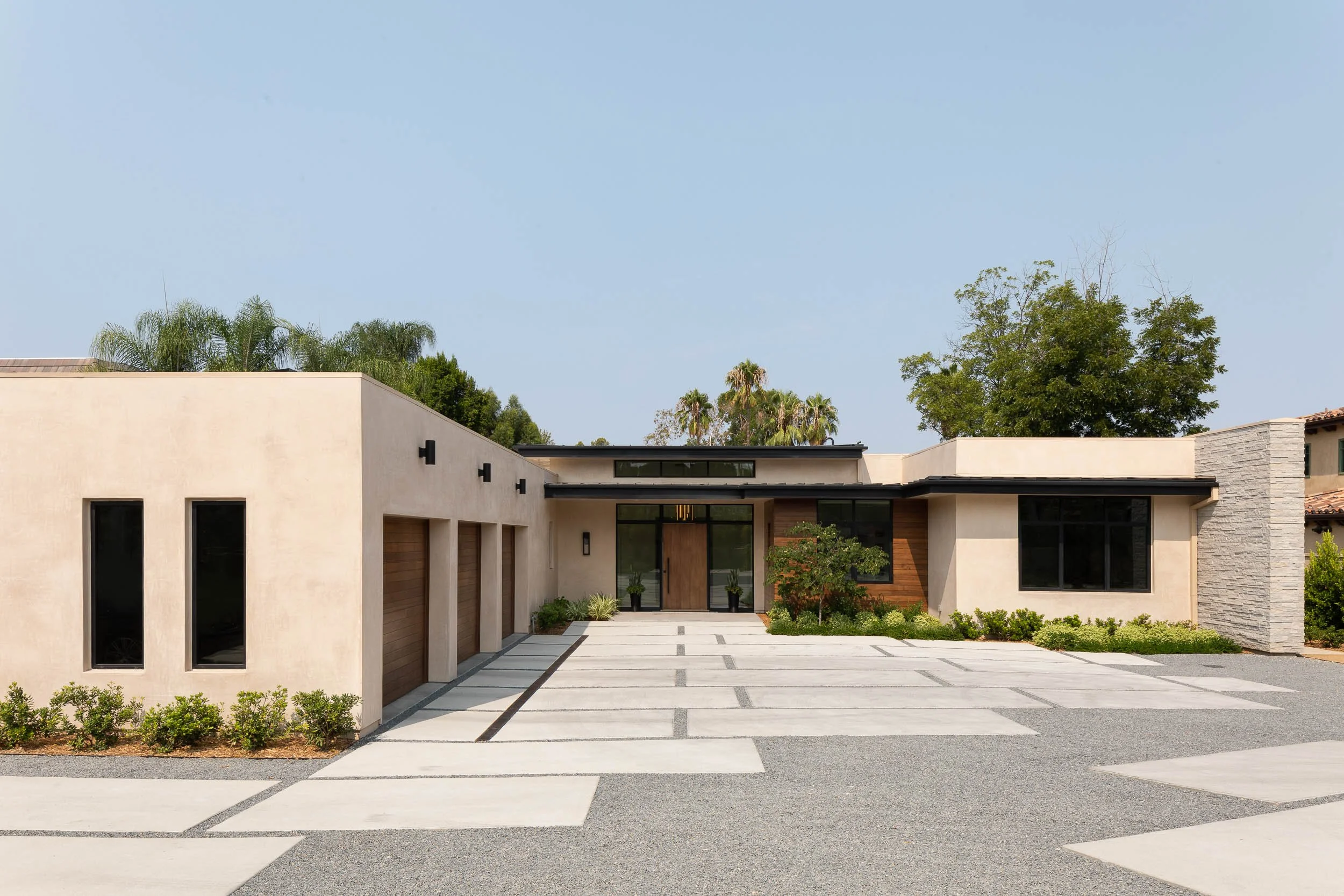 Modern house with a minimalist design, large front driveway with concrete pavers, and landscaped greenery.
