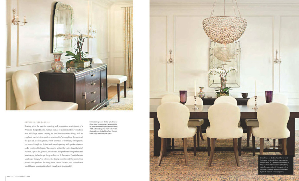 A dining room with a large wooden table surrounded by six cream-colored upholstered chairs, a chandelier overhead, and a black sideboard with decorative vases and a mirror on the wall.