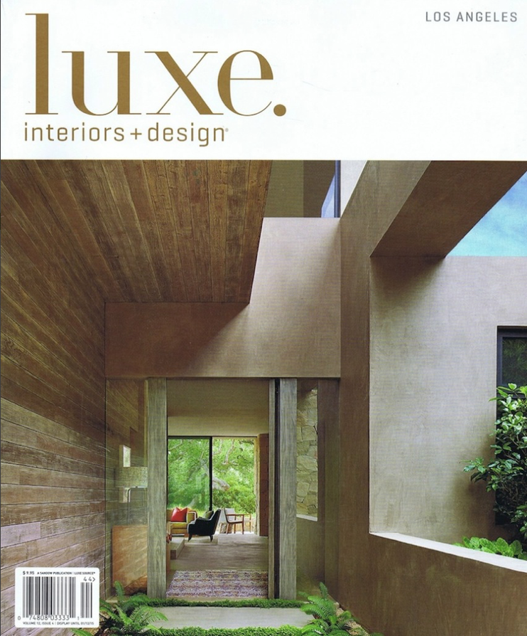 Interior view of a modern home with wooden and concrete walls, large window, and sitting area with chairs and a view of trees outside.
