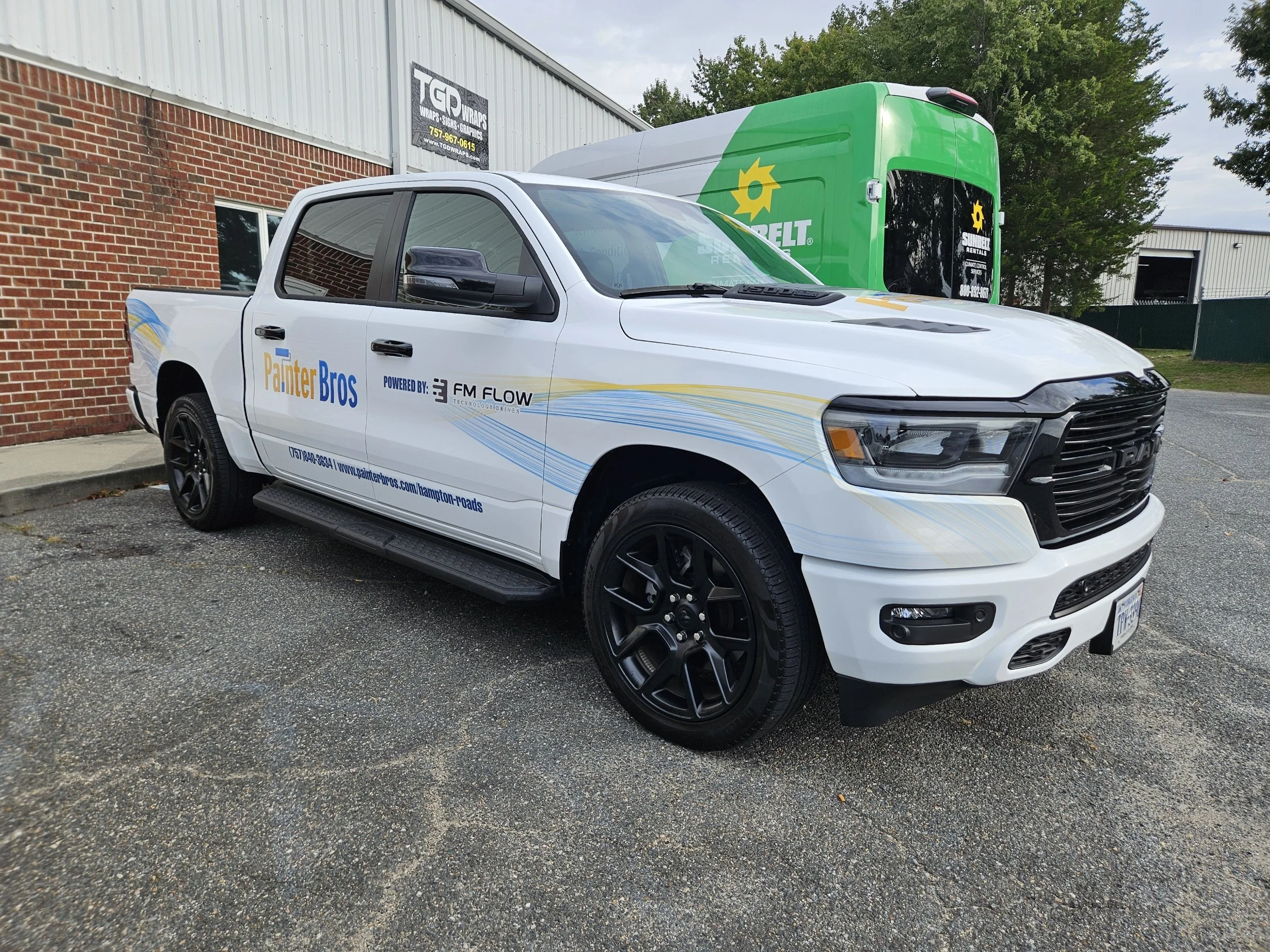 White pickup truck with decals on side promoting Painter Bros, parked in front of a brick building. A green box truck with Sunbelt Rental branding is visible in the background.