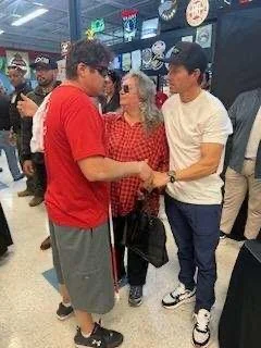 John and Mark Wahlberg engaged in conversation. The Mark Wahlberg on the right is wearing a white shirt and jeans, and the John on the left is wearing a red shirt and grey shorts.