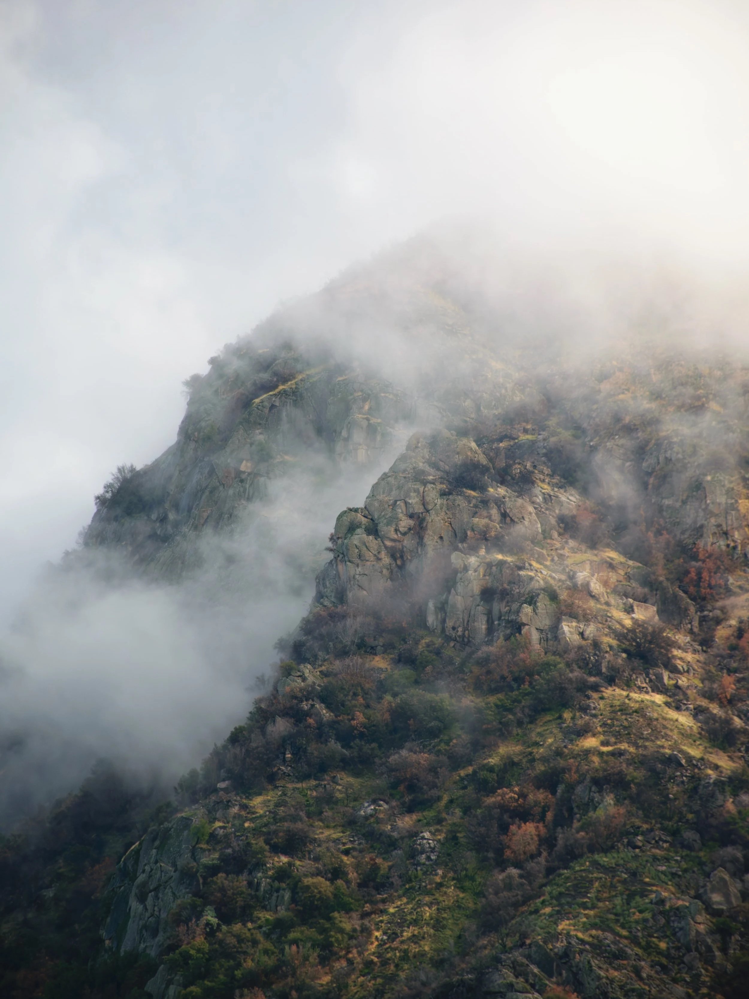 Mist-shrouded mountain with rocky cliffs and sparse vegetation.