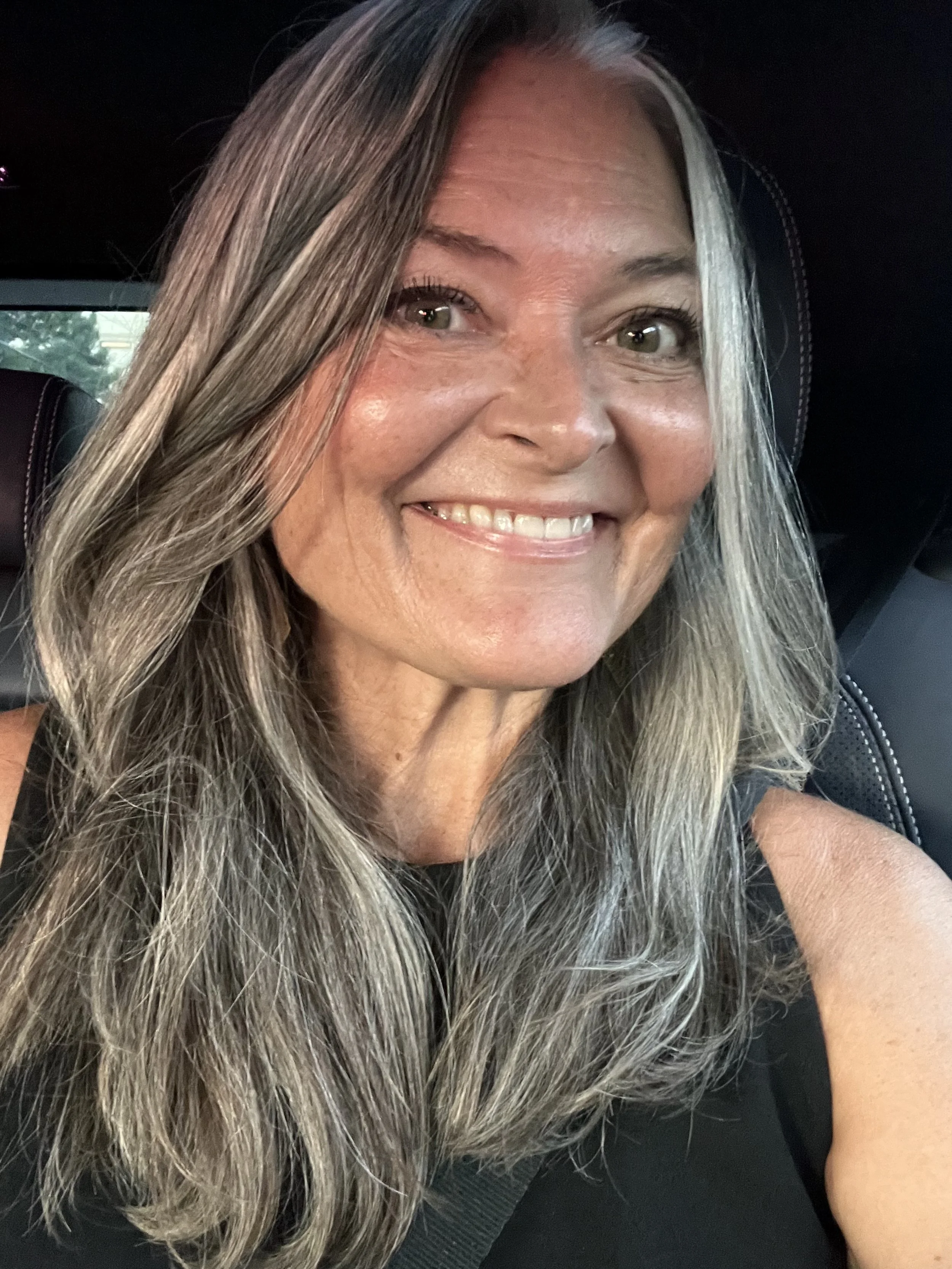 Close-up of a smiling woman with long, wavy, gray hair and hazel eyes.
