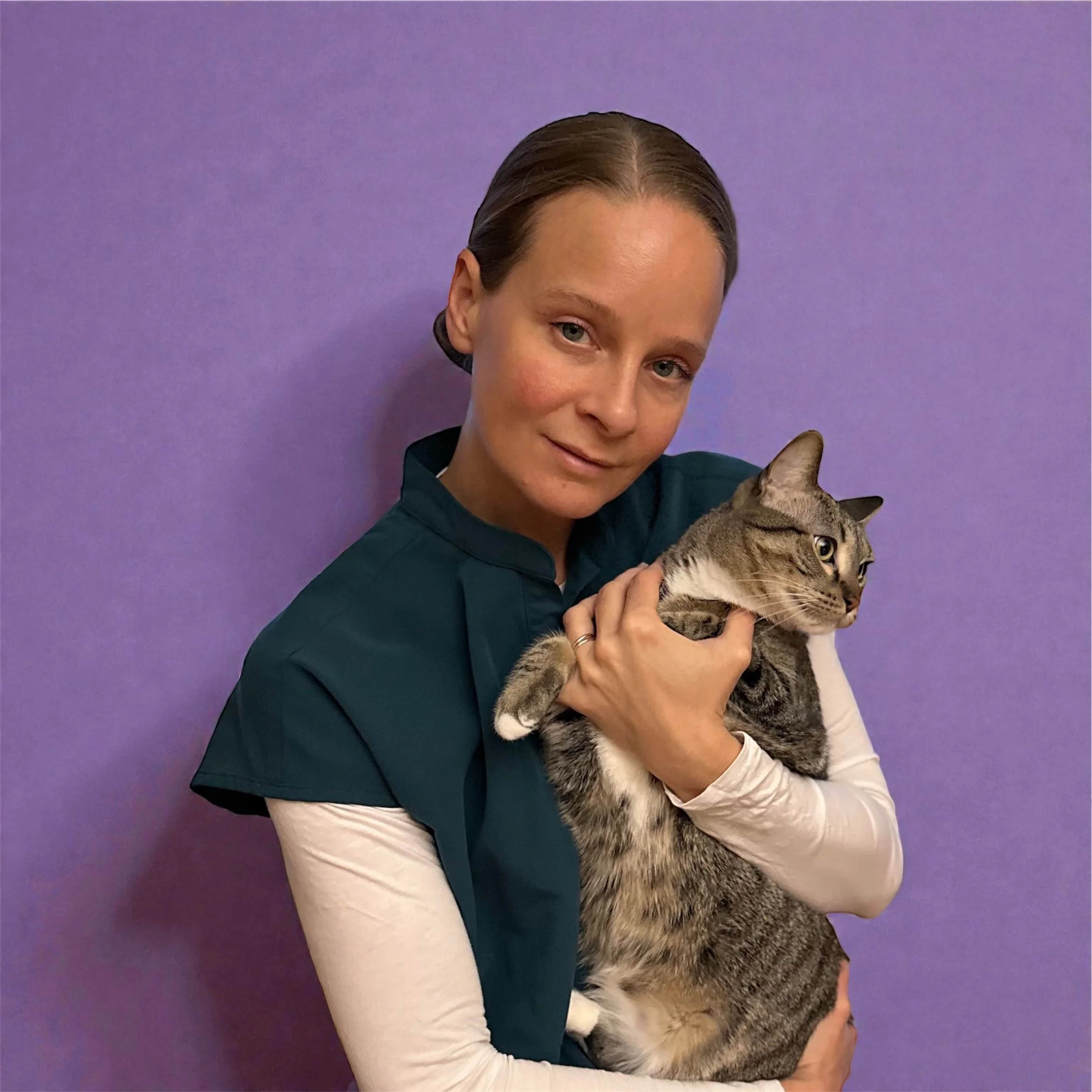 A woman holding a gray tabby cat against a purple background.