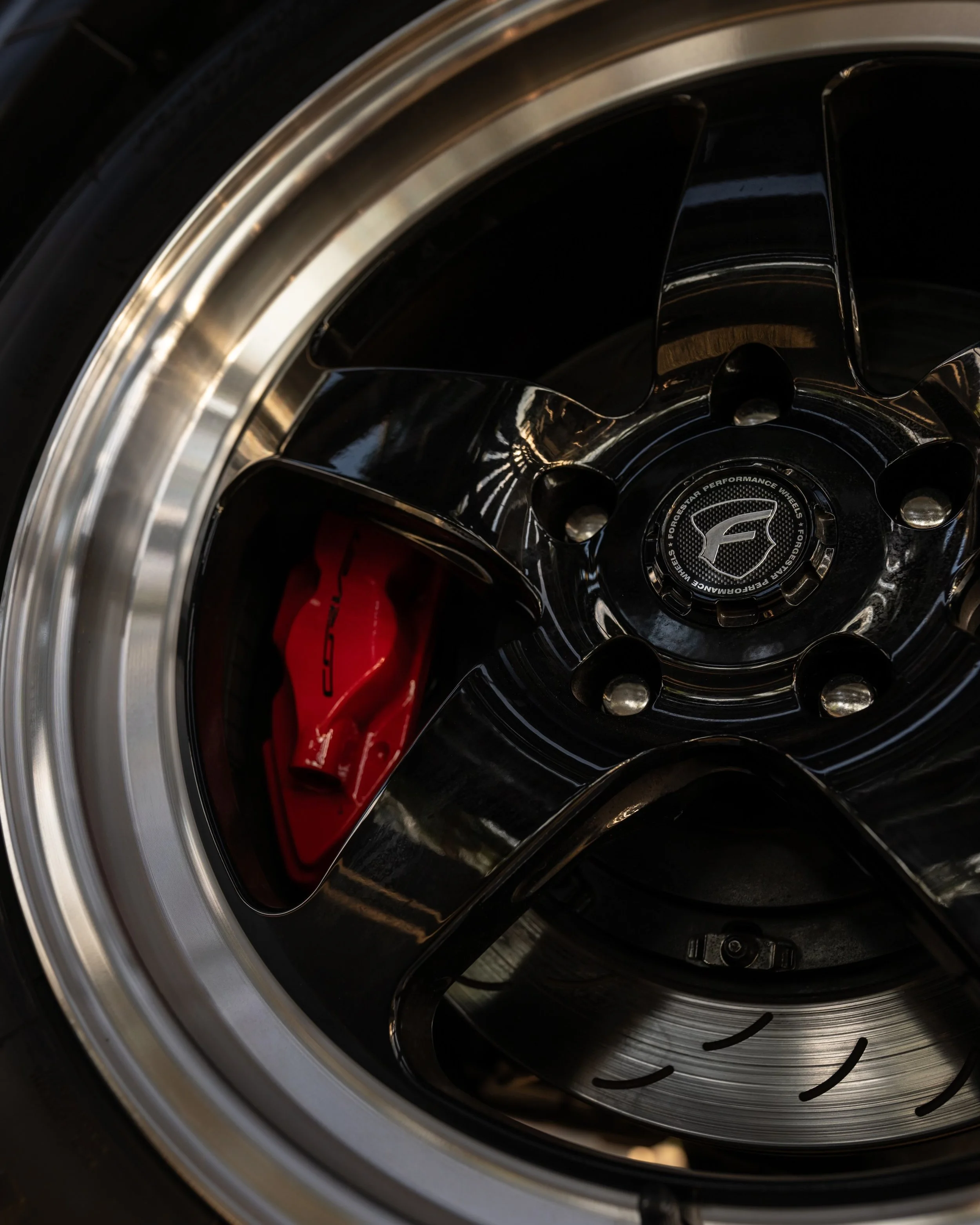 Close-up of a car wheel with a black alloy rim and red brake caliper visible through the rim spokes.