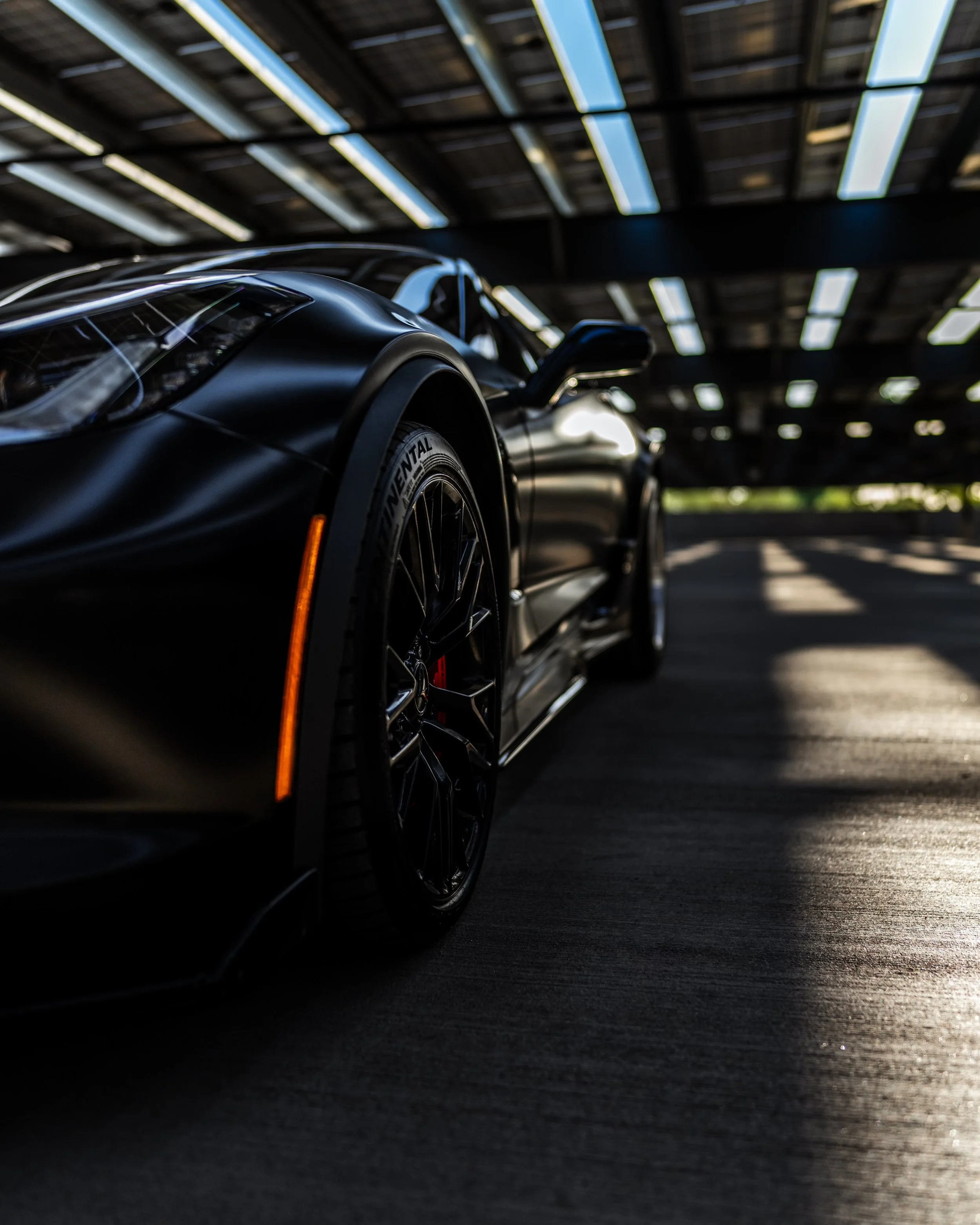 Close-up of a sleek black sports car inside a modern parking garage, with sunlight streaming in from above.