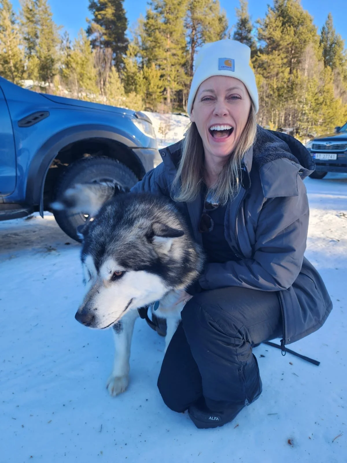 A woman smiles while petting a husky.