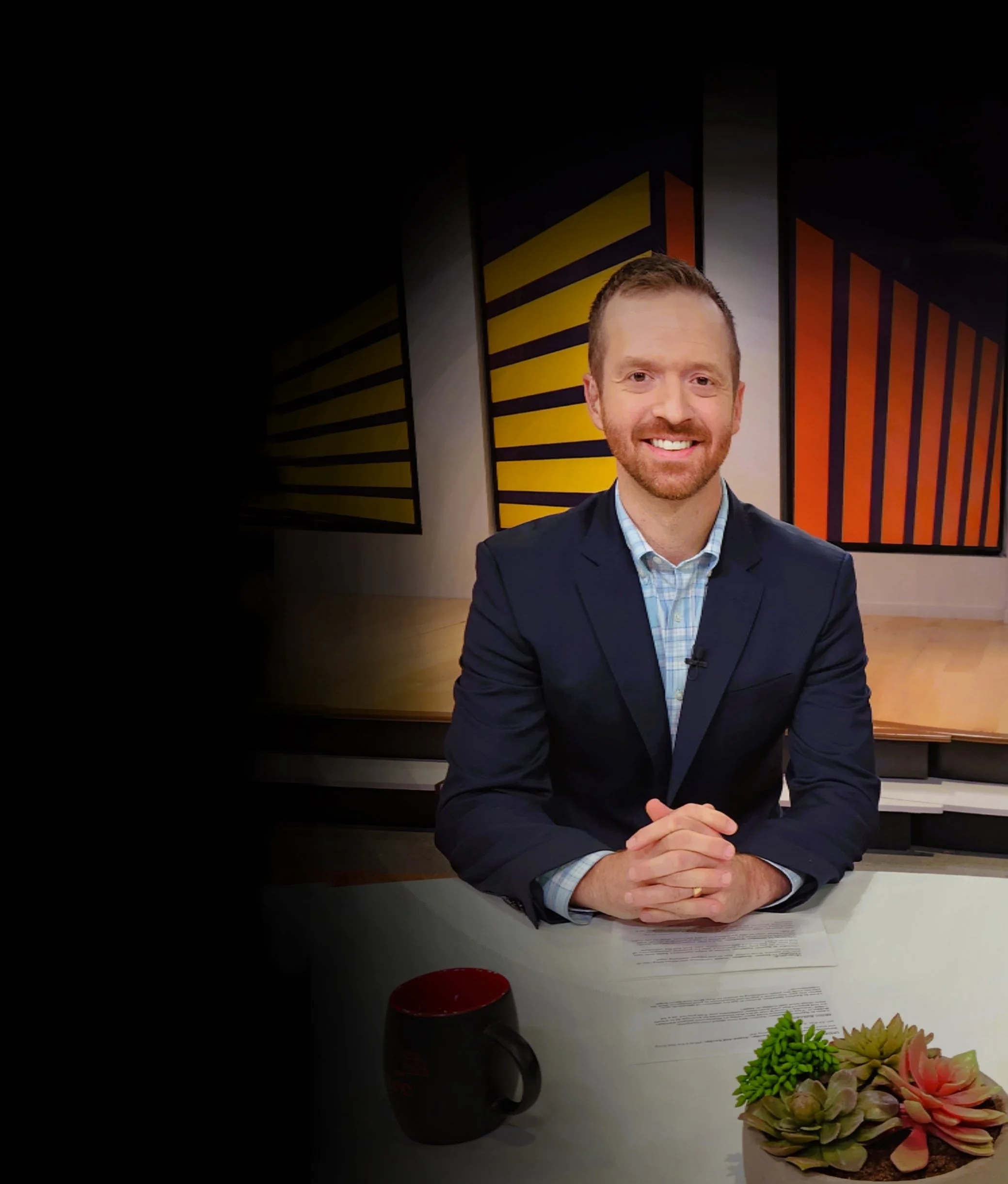 Jonathan Block wearing a dark suit, sitting at a table with hands clasped, smiling at the camera hosting PwC's Trust in Action webcast on Artificial Intelligence.