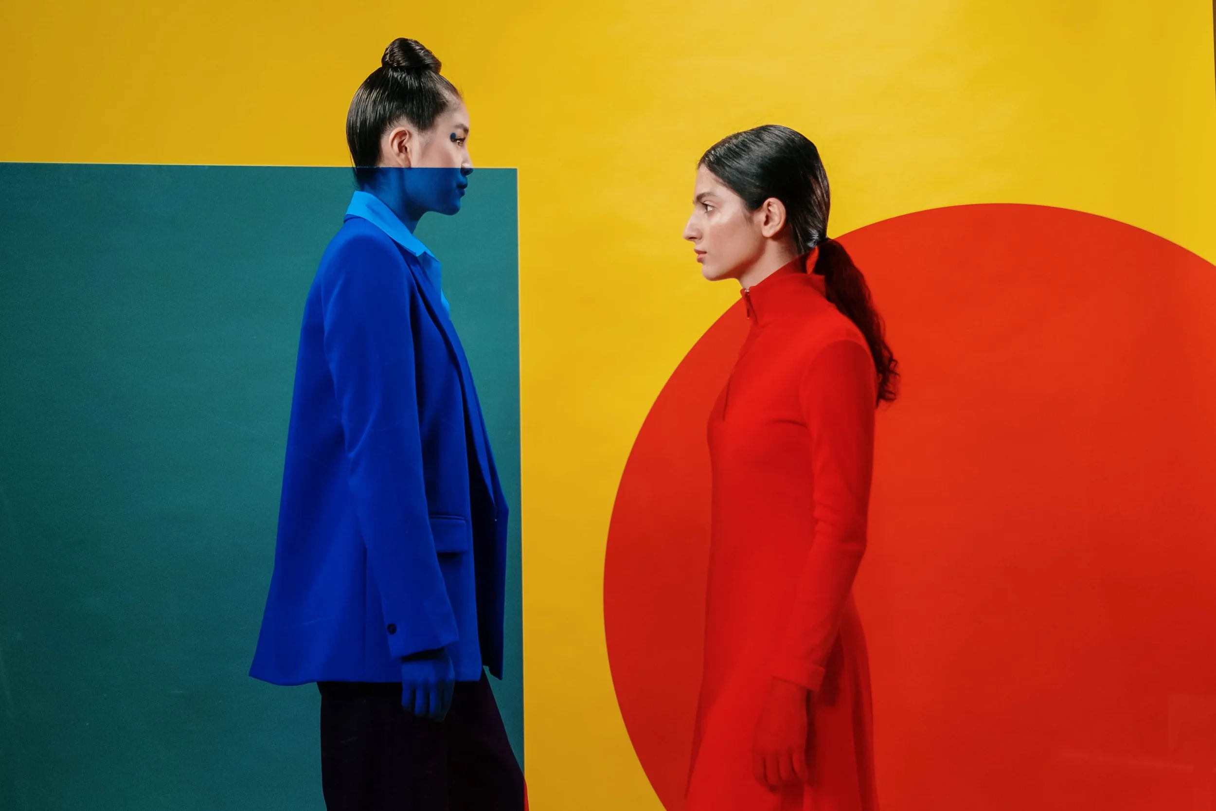 Two figures in red and blue suits face each other against a bold geometric background.