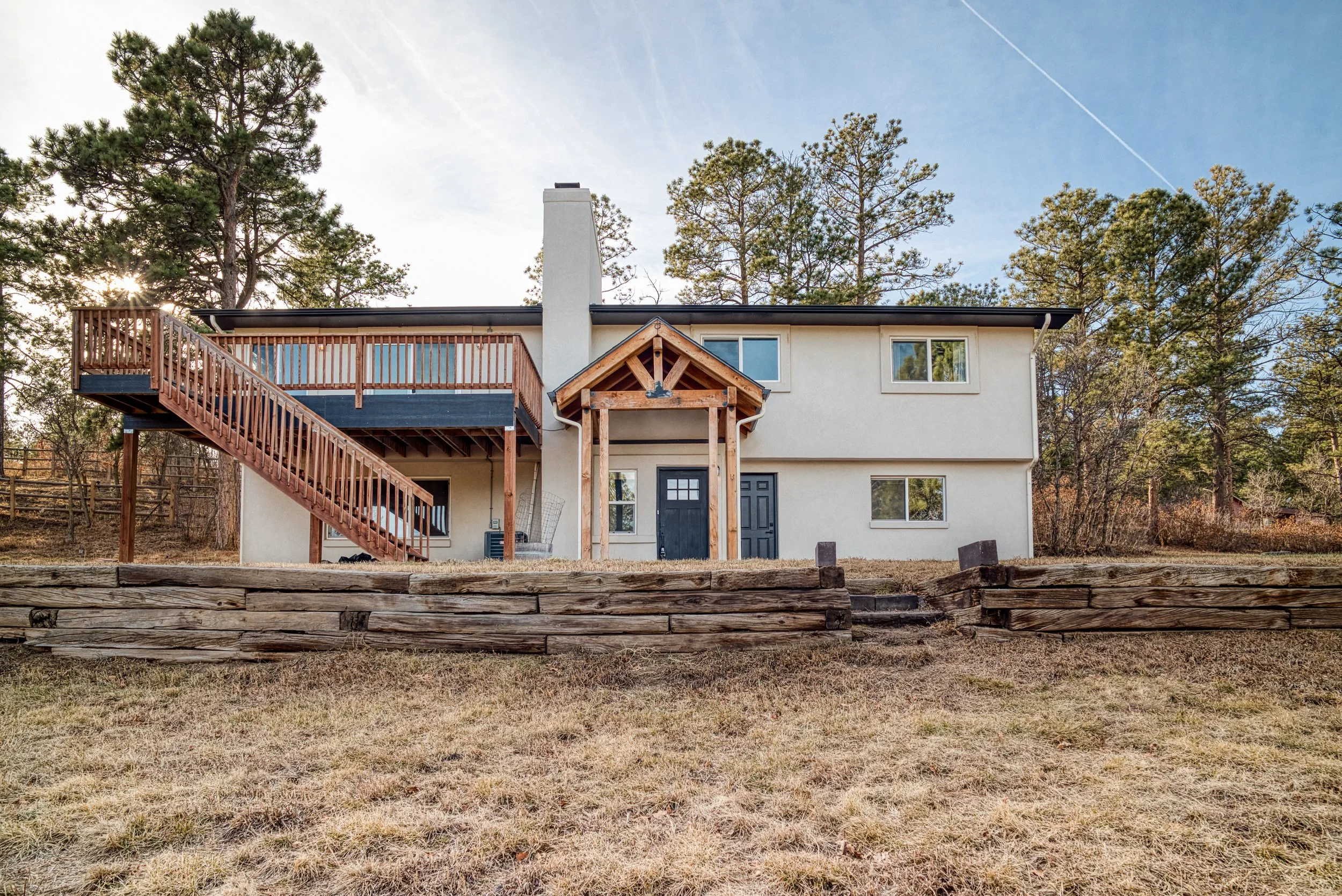 Front exterior of a renovated house featuring a wooden porch entry and neutral siding under a clear sky.