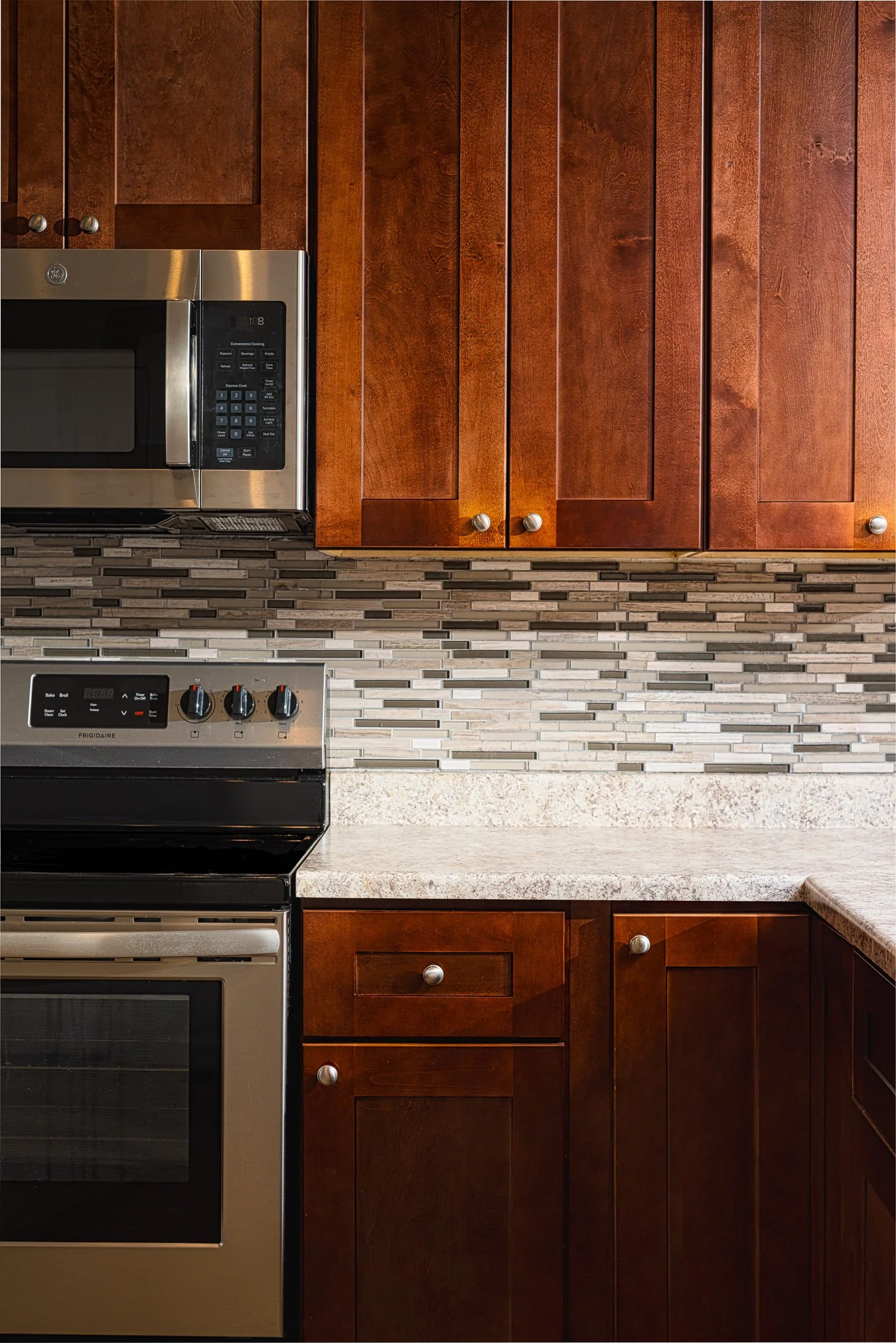 Detail shot of dark wood kitchen cabinets paired with a decorative tiled backsplash and granite countertops.