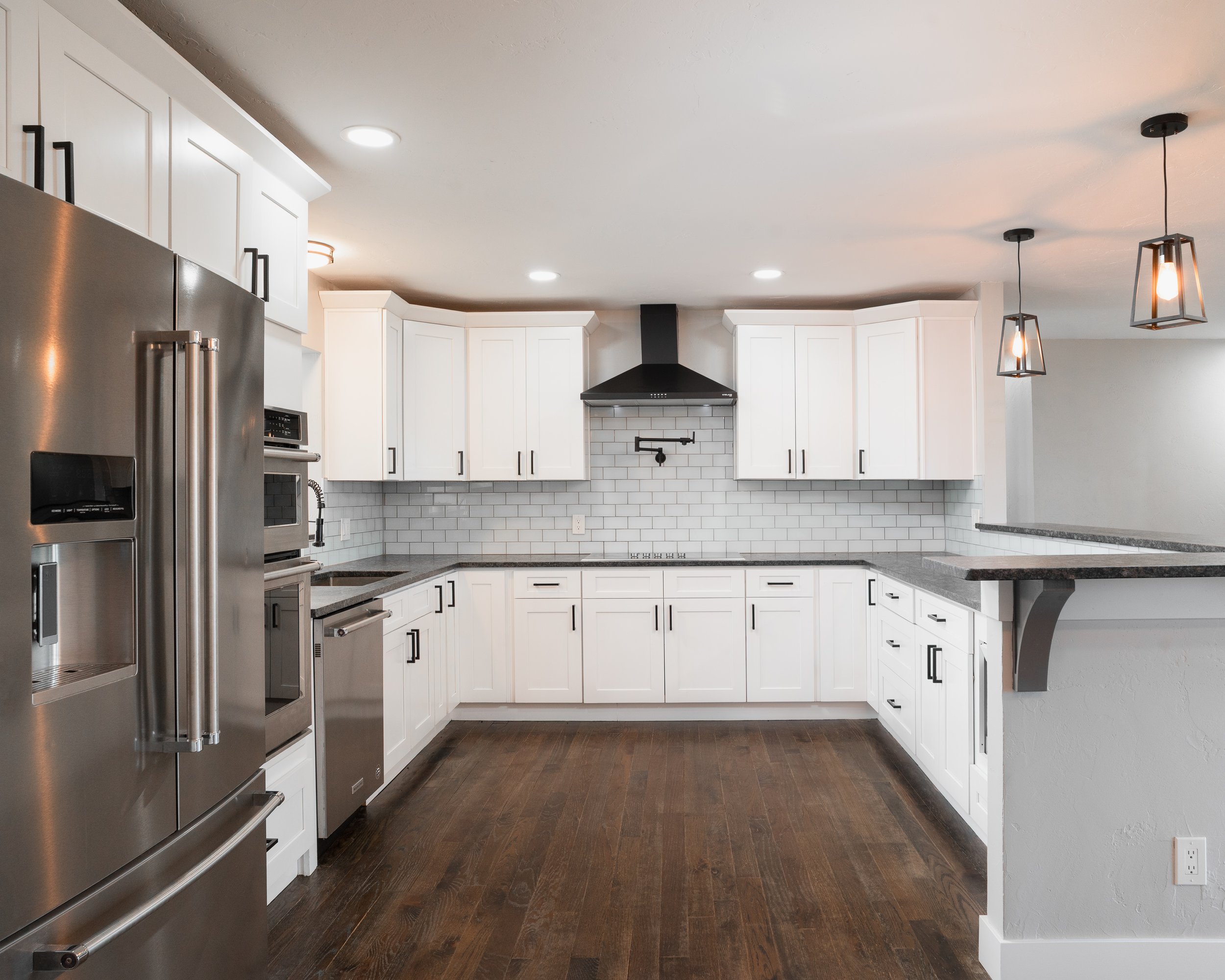 U-shaped kitchen layout featuring white cabinetry, a black range hood, and integrated stainless steel wall ovens.