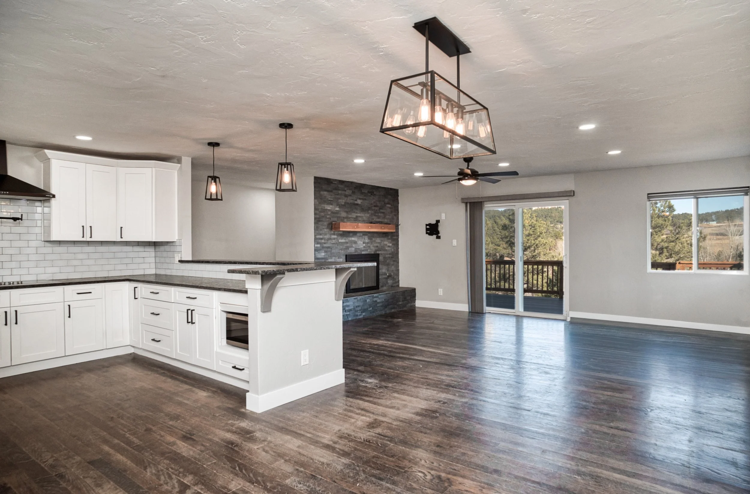 Spacious open-plan room with a modern chandelier, stone fireplace, and polished concrete or dark tile flooring.