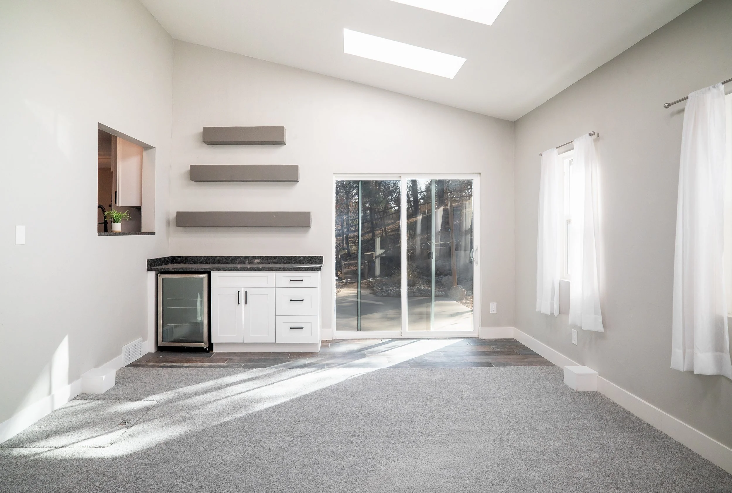 Sunlit dining area or bonus room with grey floating shelves, a beverage cooler, and large sliding glass doors.