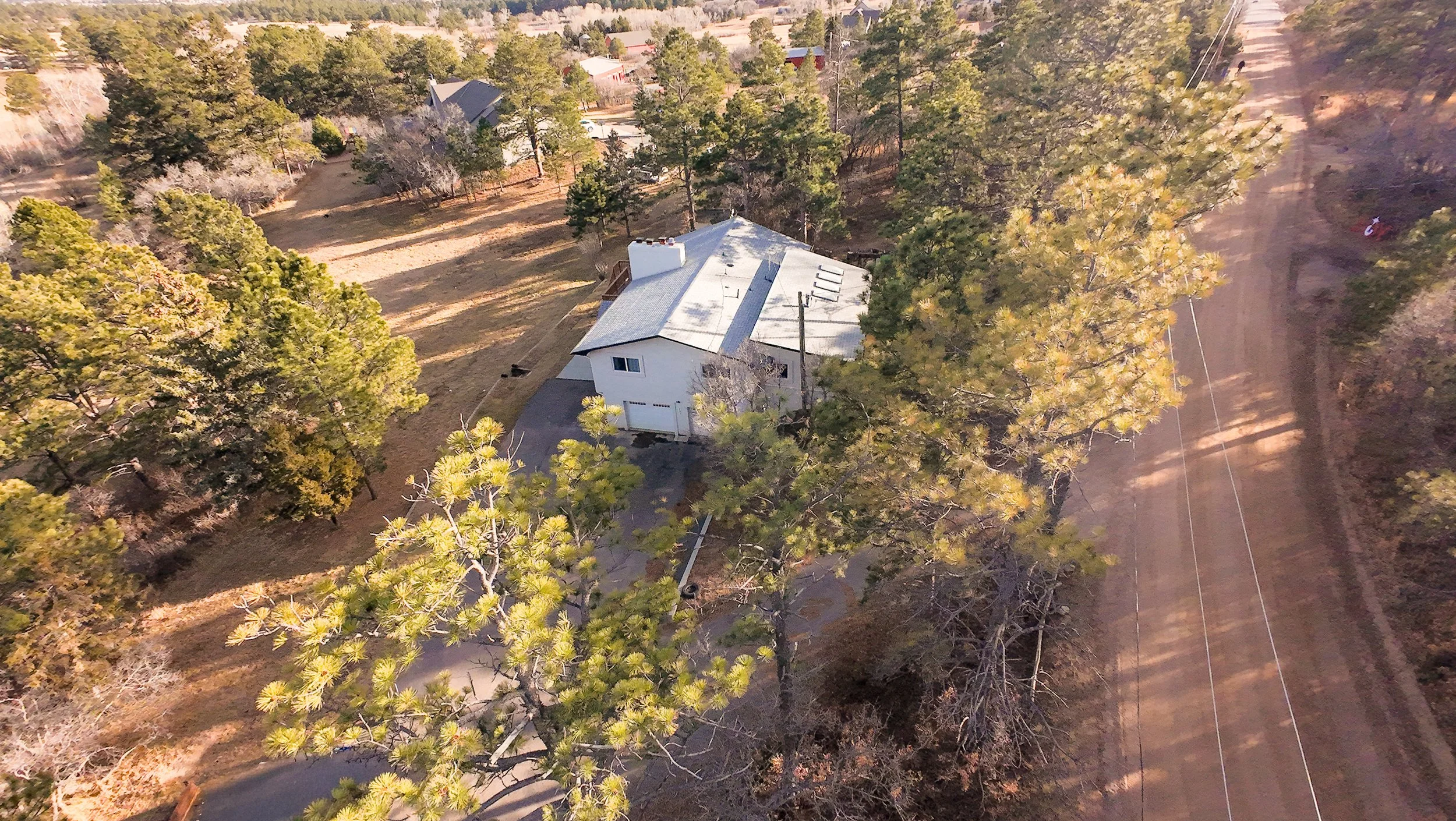 Aerial view of a residential home surrounded by native evergreen trees in Colorado Springs, CO.