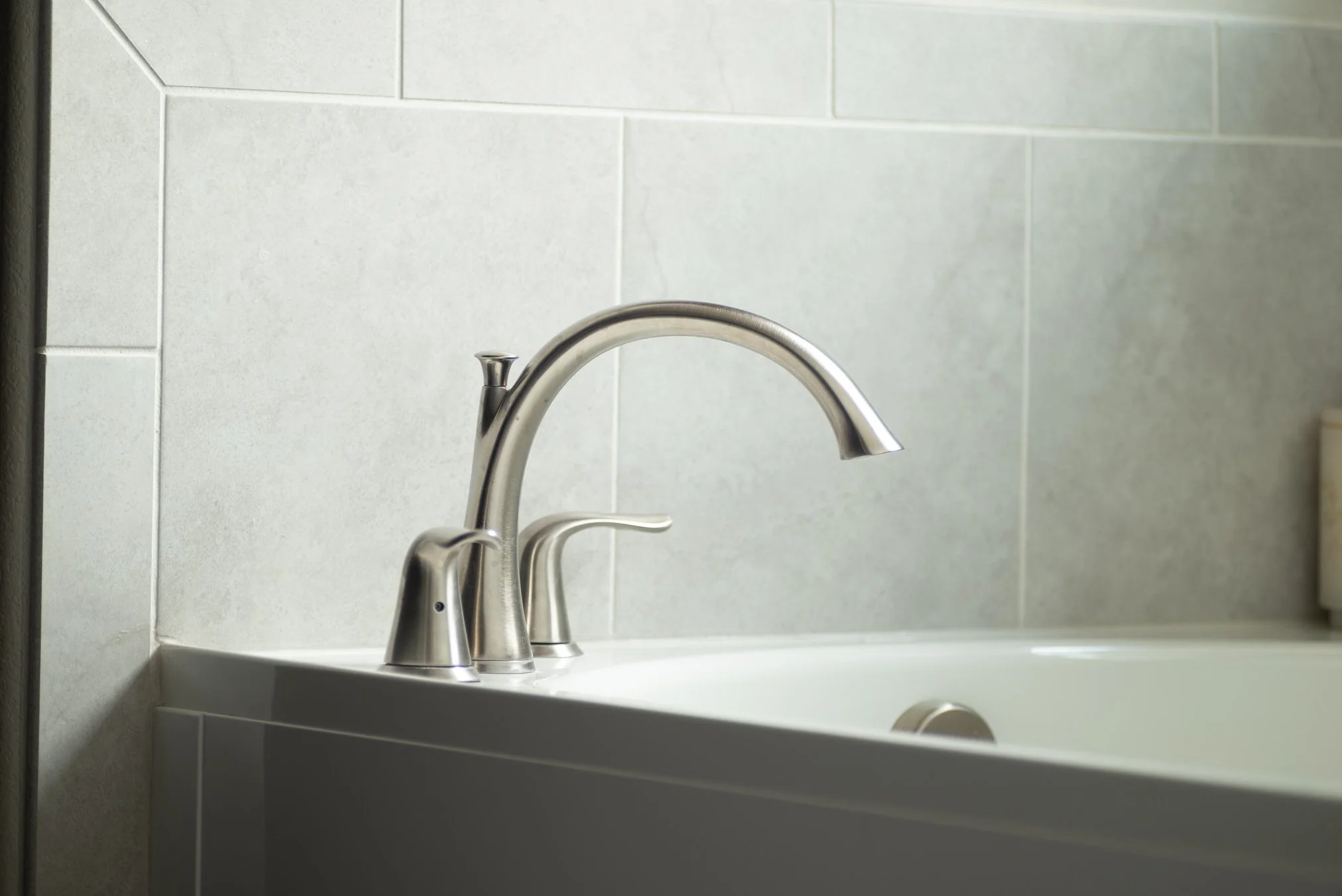 HDR detail photography of a brushed nickel two-handle bathroom faucet mounted on a white soaking tub, set against large format gray marble-look tile surround — professional real estate and interior detail photography by Peak Exposure, Colorado Spring