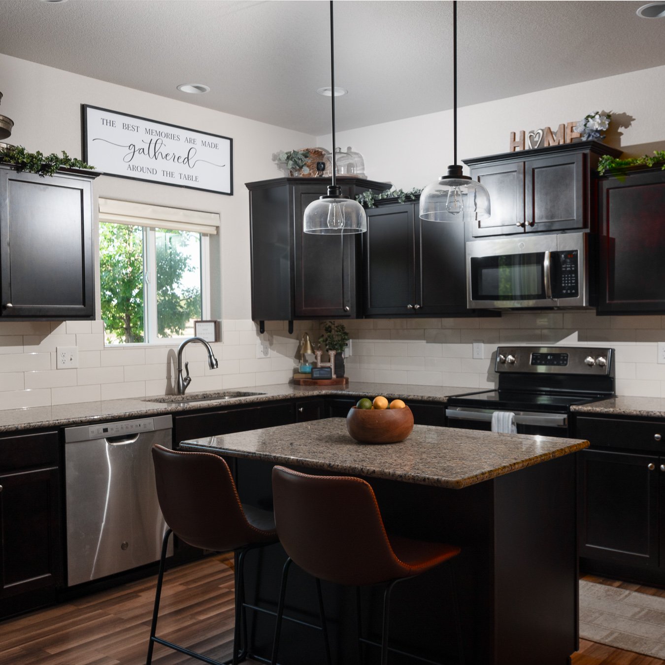 Professionally photographed kitchen featuring dark espresso cabinetry, granite countertop island with leather bar stools, subway tile backsplash, and industrial pendant lighting — Colorado Springs real estate photography by Peak Exposure