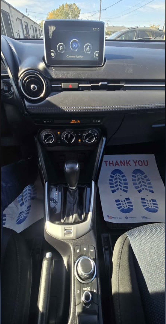 Interior of a car showing the dashboard, center console with gear shift, climate controls, infotainment screen, and floor mats with a thank you message and footprints.