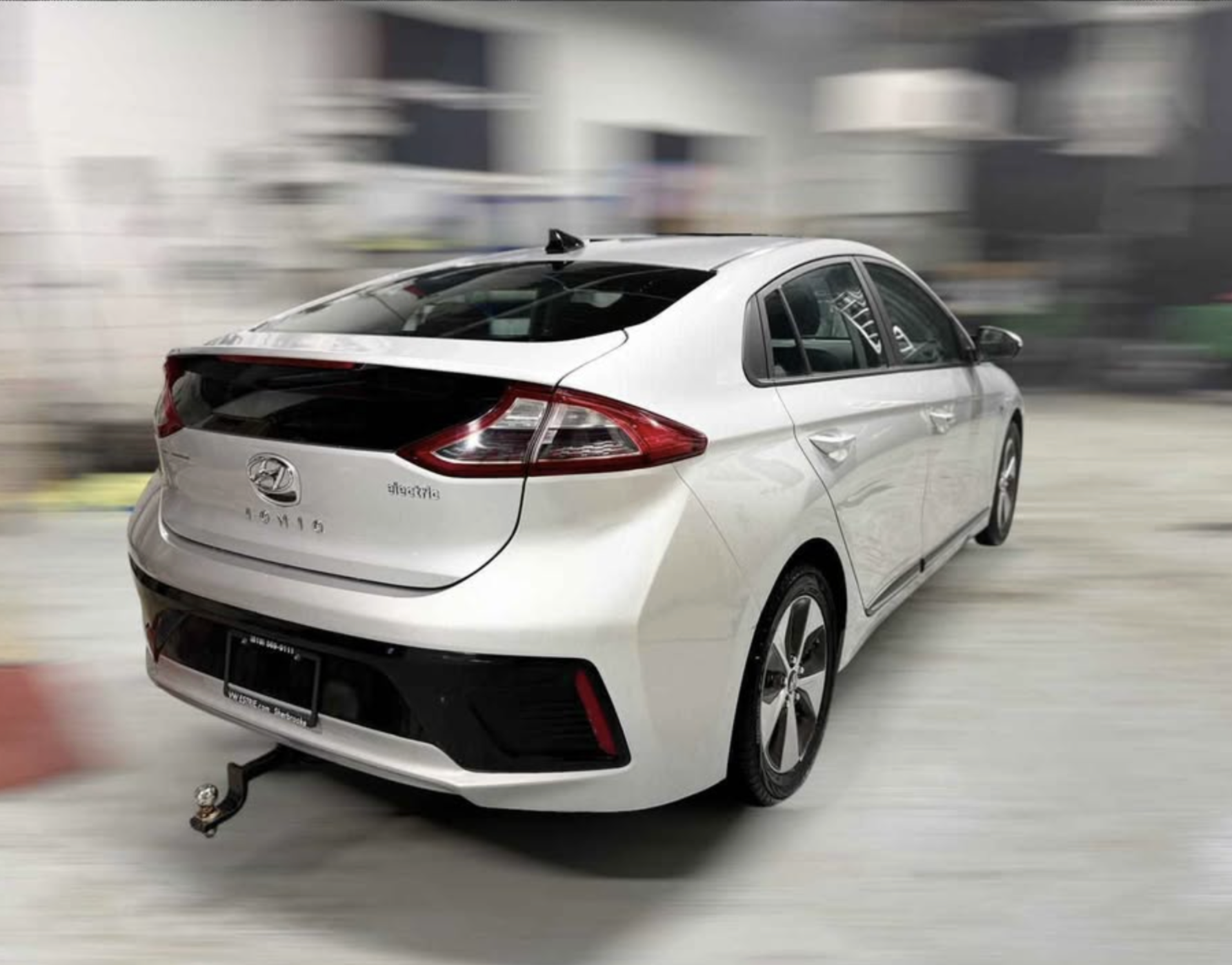 White modern sedan car parked indoors with a trailer hitch, and a blurred background.