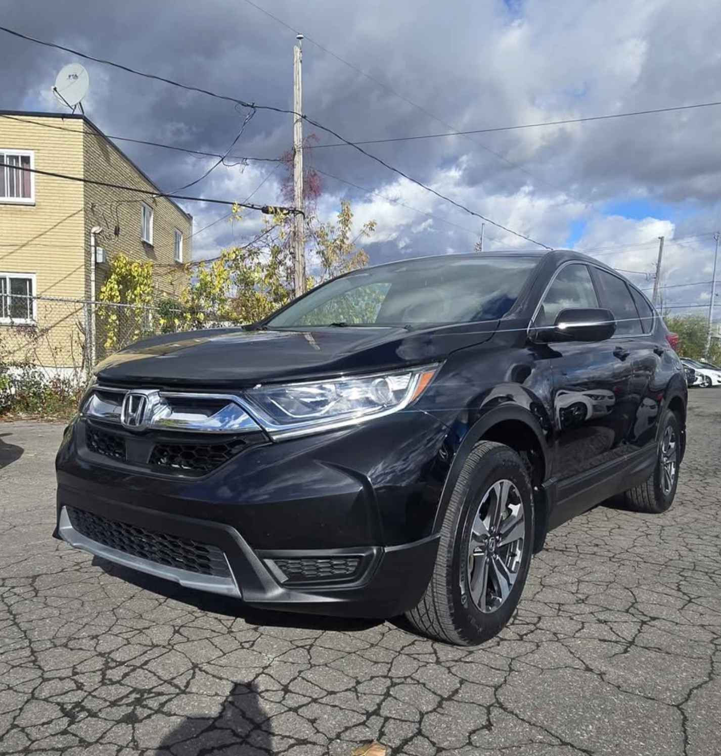 Black Honda SUV parked on cracked pavement with cloudy sky and residential buildings in the background.