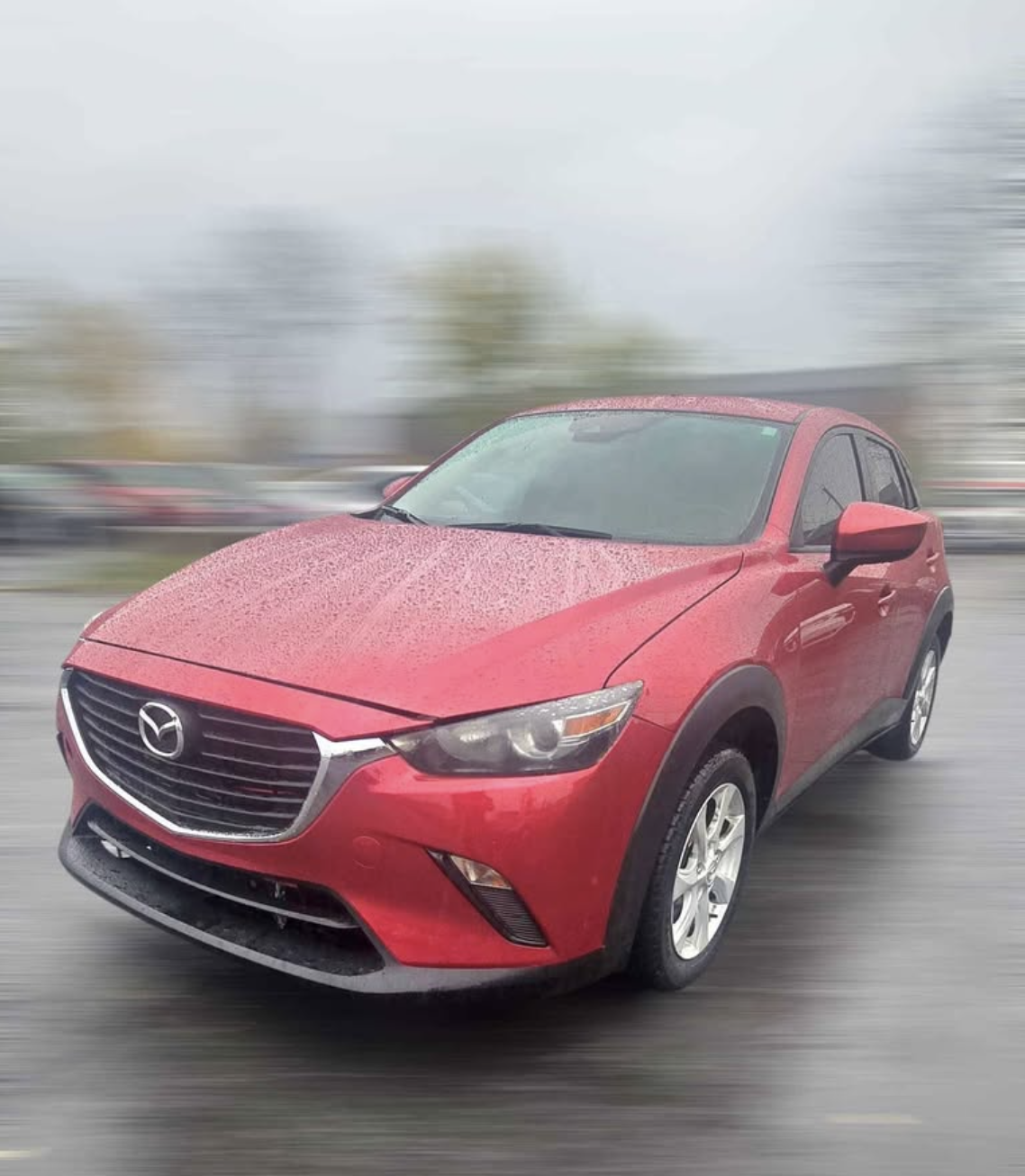 Red Mazda SUV driving on a wet road with rain droplets on the windshield and motion blur in the background.