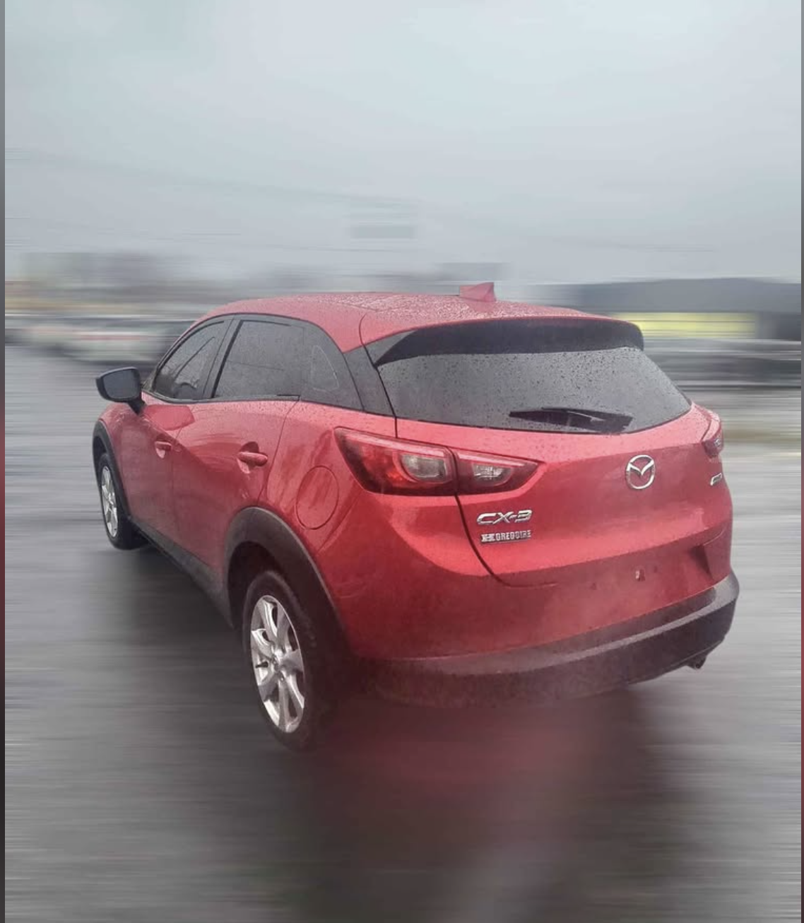 Red Mazda CX-3 on a rainy road with raindrops and blurred background.