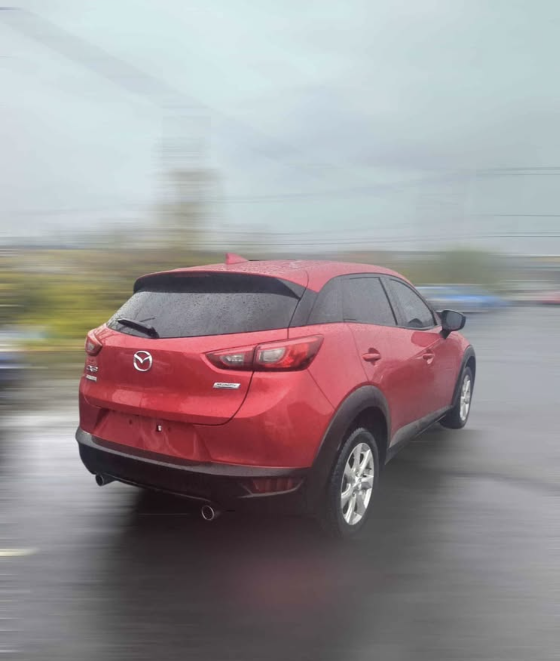 Red Mazda SUV driving in rainy weather with blurred background.