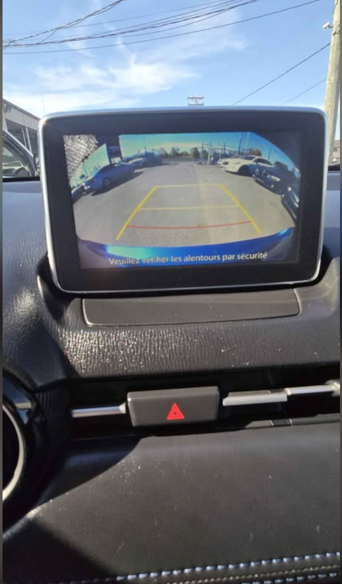 Car's rearview camera display showing parking lot with parked cars, yellow and red guiding lines, and a blue weather warning message in French.