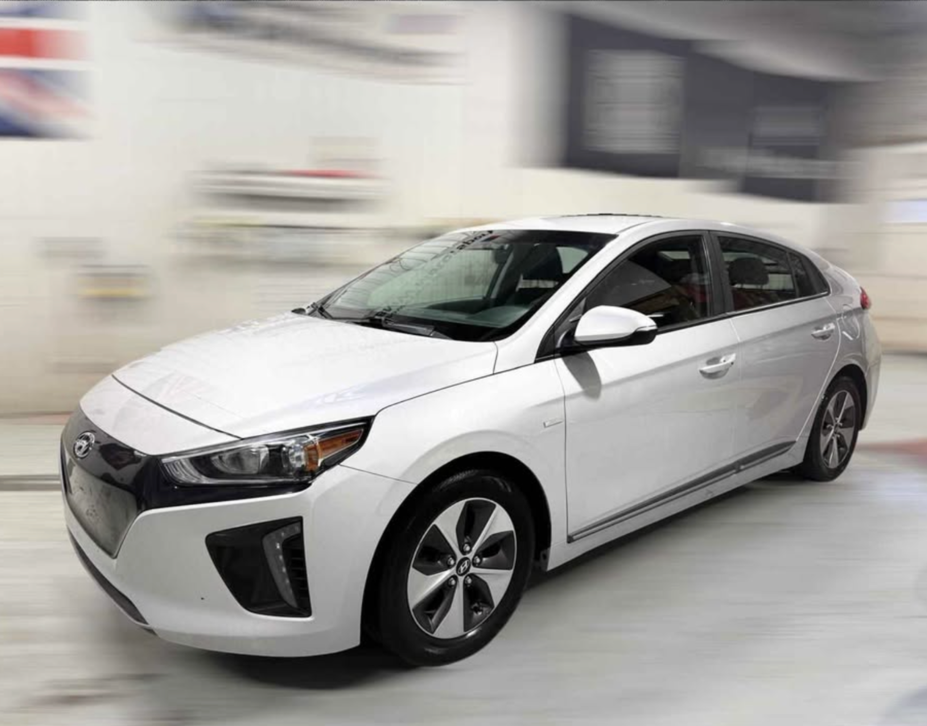 A white sedan car on a dealership or garage floor, slightly blurred background.