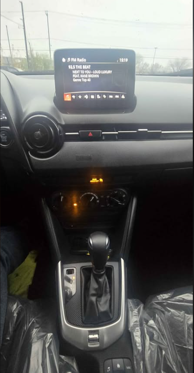 Inside view of a car dashboard showing a radio screen tuned to FM radio station 92.5 THE BEAT, displaying song info and time, with the gear shift in the center console.