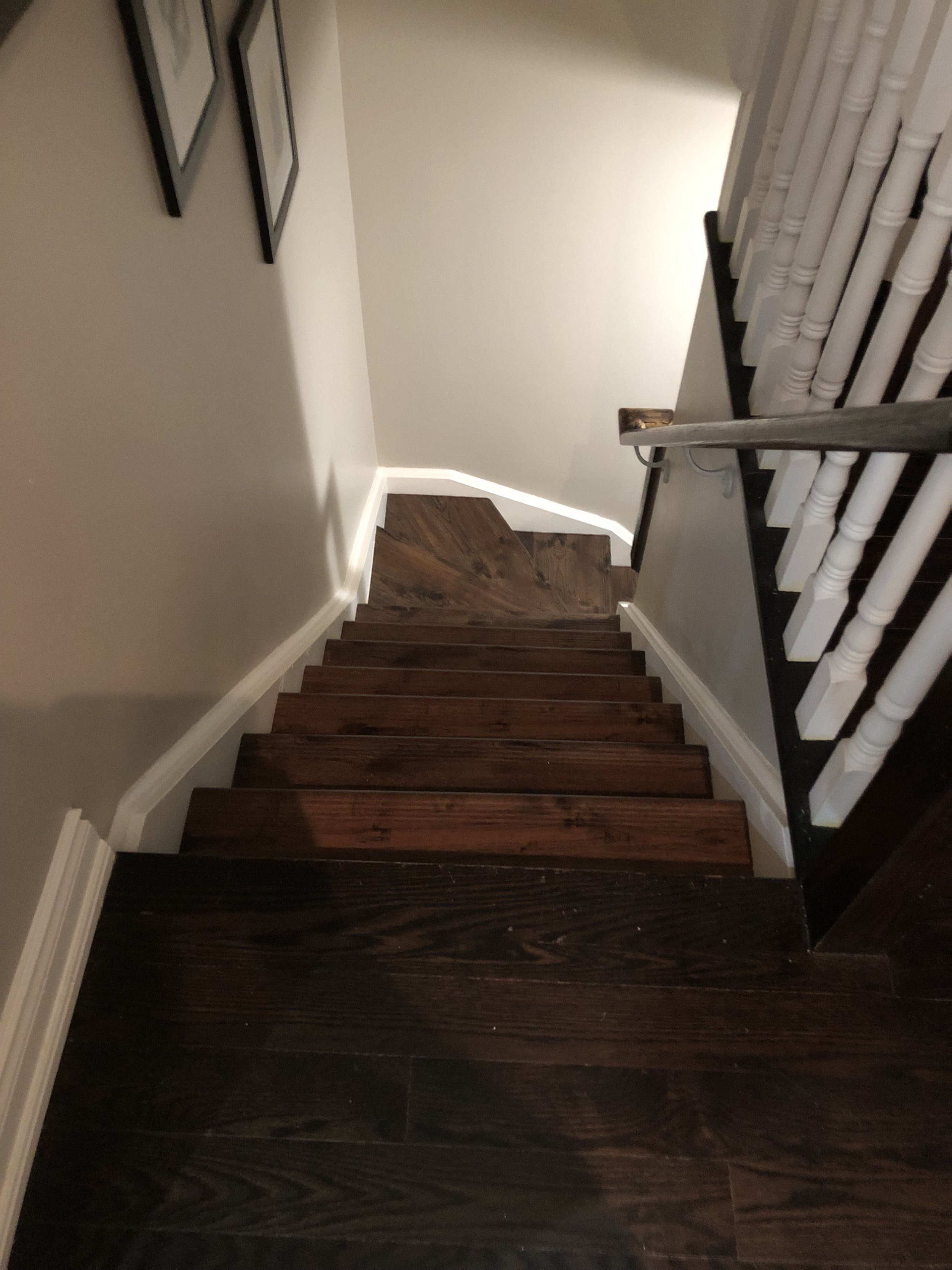 Wooden staircase from top view, showing dark and light brown steps, white walls, and framed pictures on the wall.