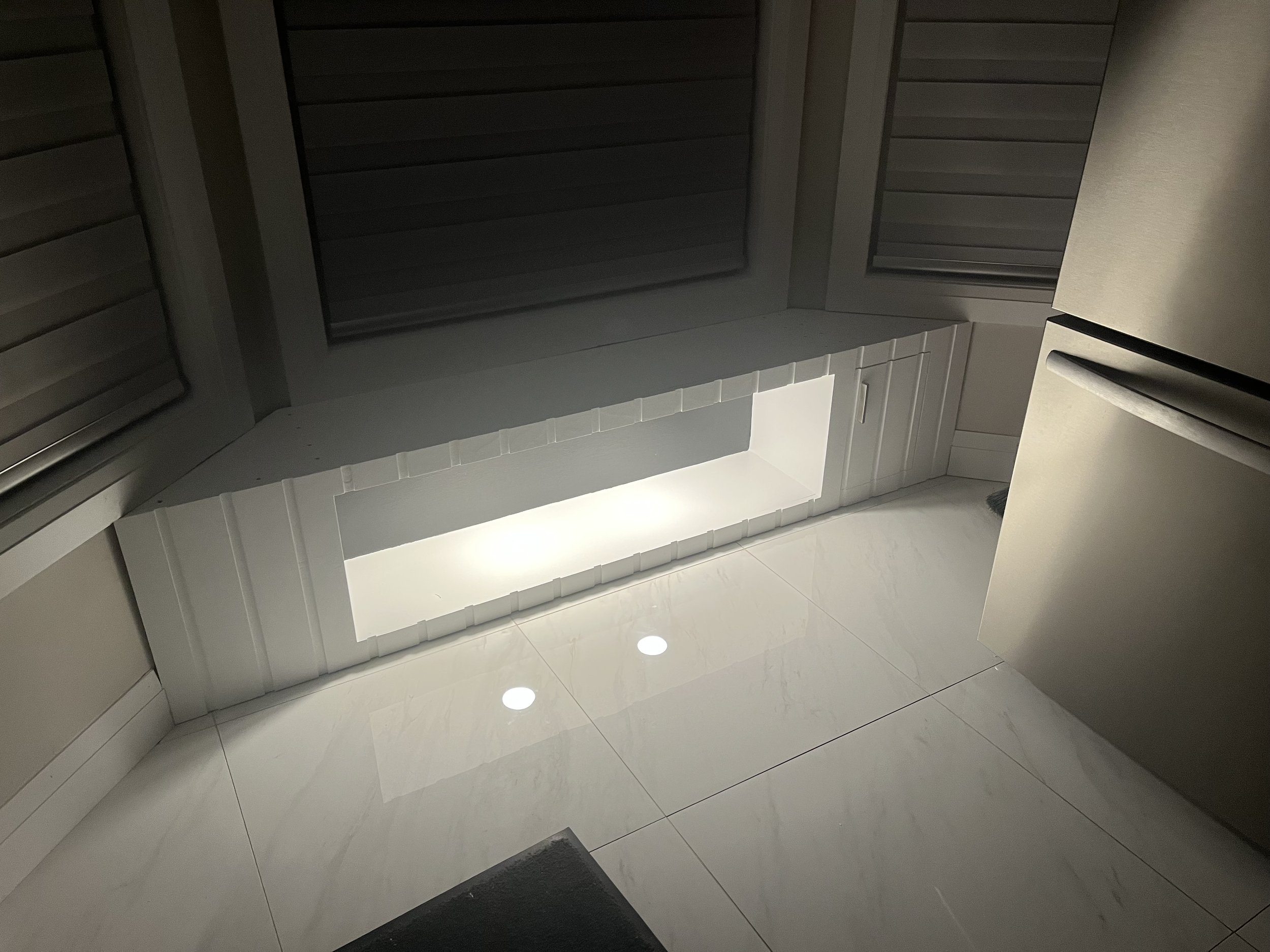 Close-up of a modern kitchen with a white tiled floor, gray cabinets, and under-cabinet lighting.