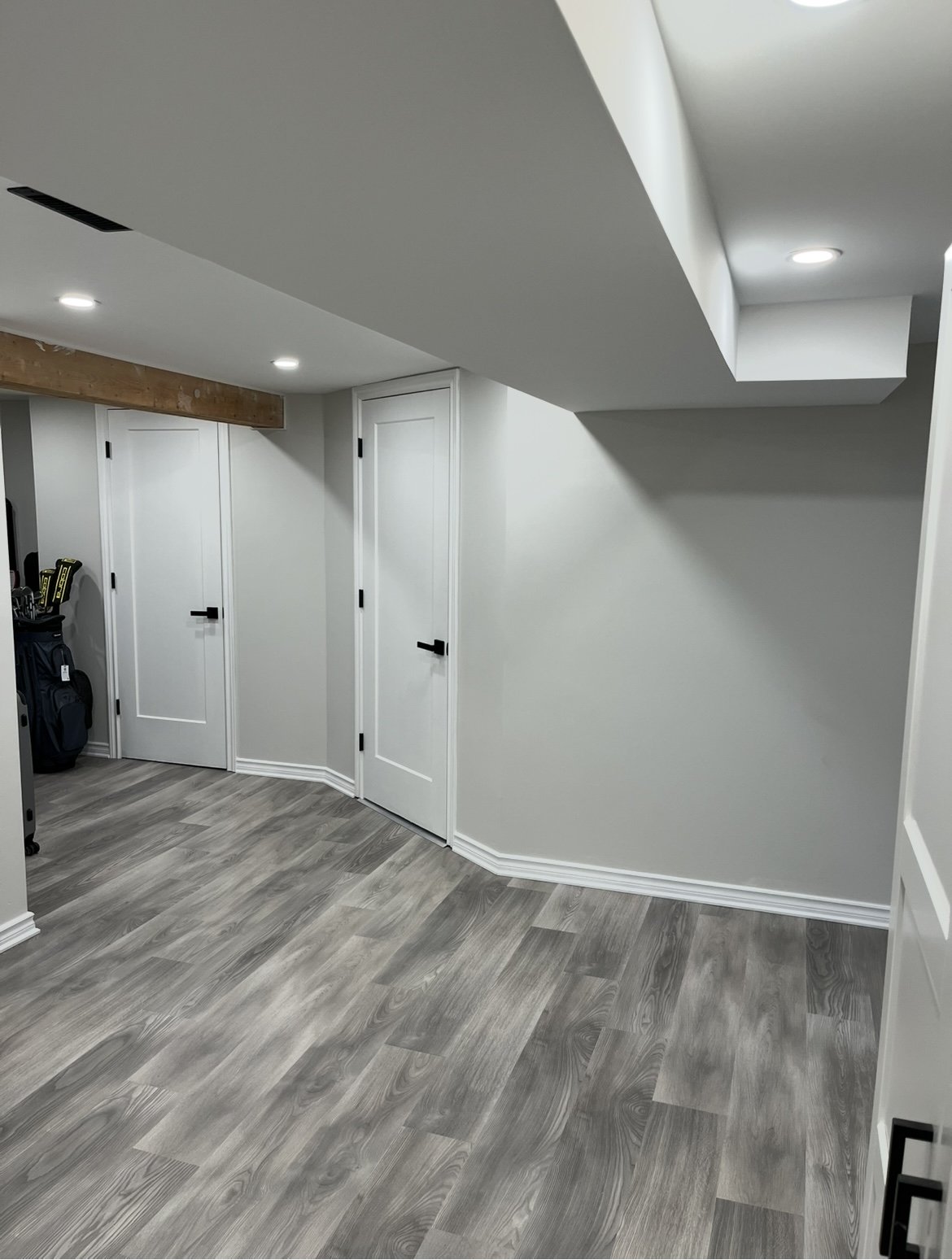 A modern room with white doors, gray wood flooring, and a ceiling with recessed lighting.