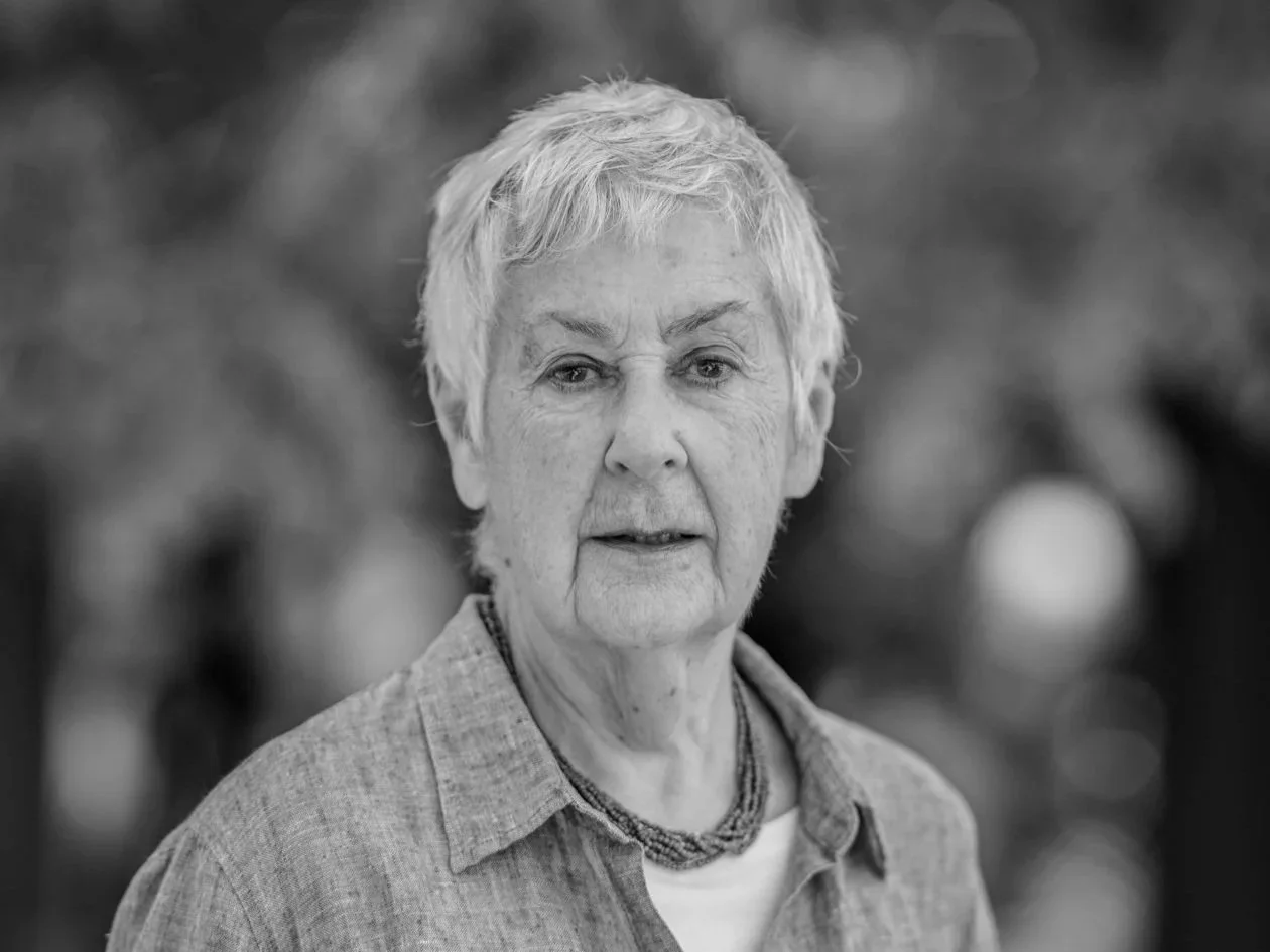 Black and white photo of short cropped haired woman looking at camera wearing open necked shirt and beads around her neck