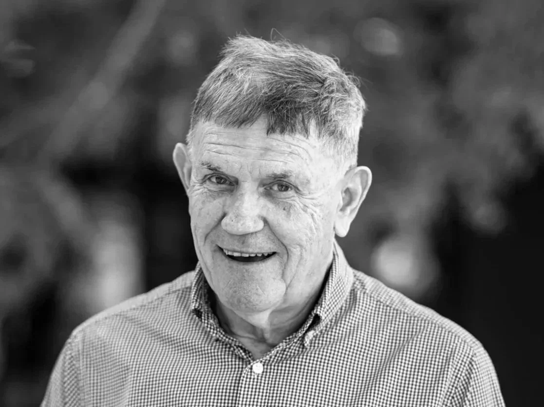Black and white photo of man with short crewcut hair, smiling at camera, wearing checked shirt