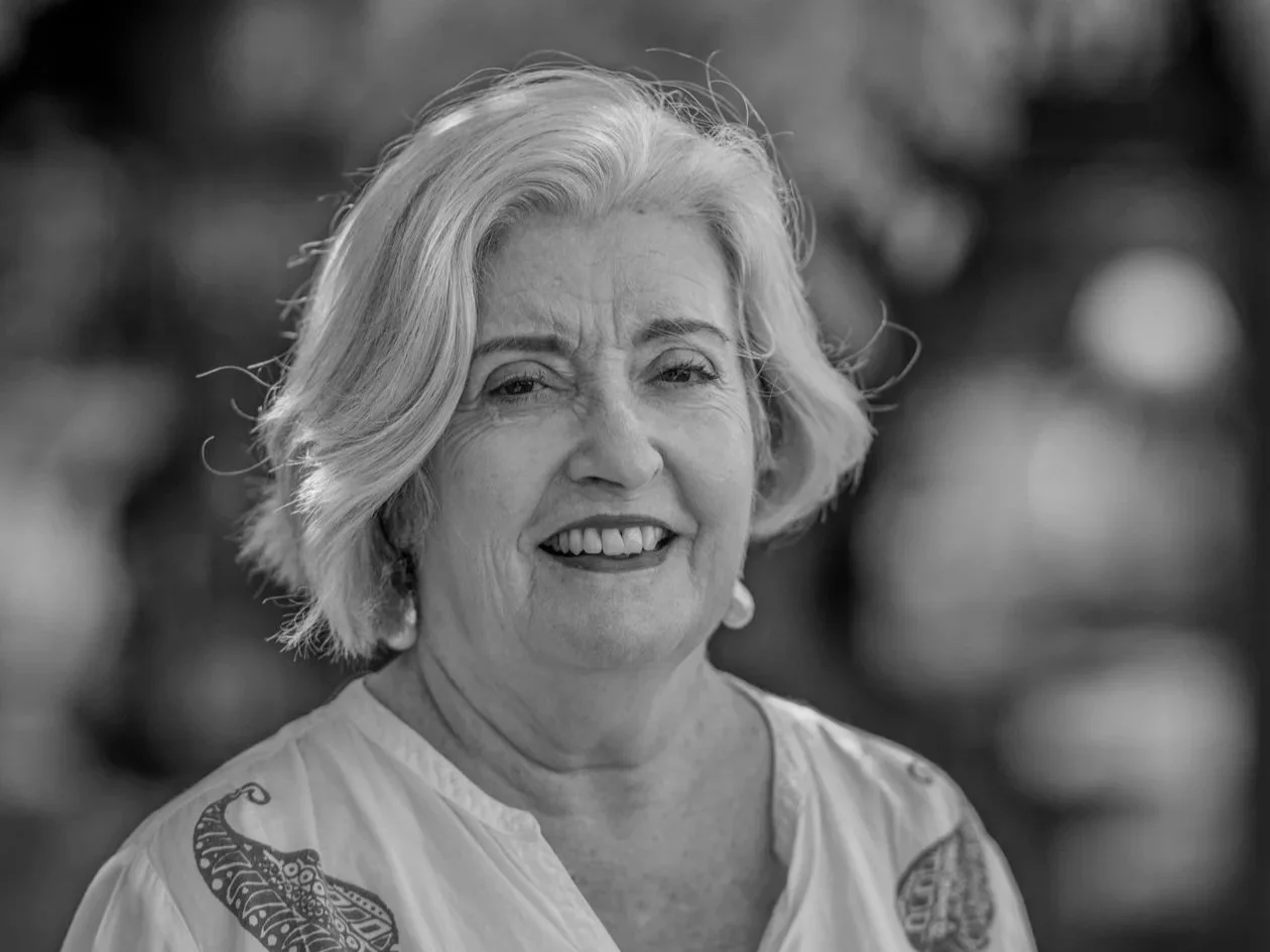 Black and white photo of grey haired woman smiling at camera wearing white open-necked shirt
