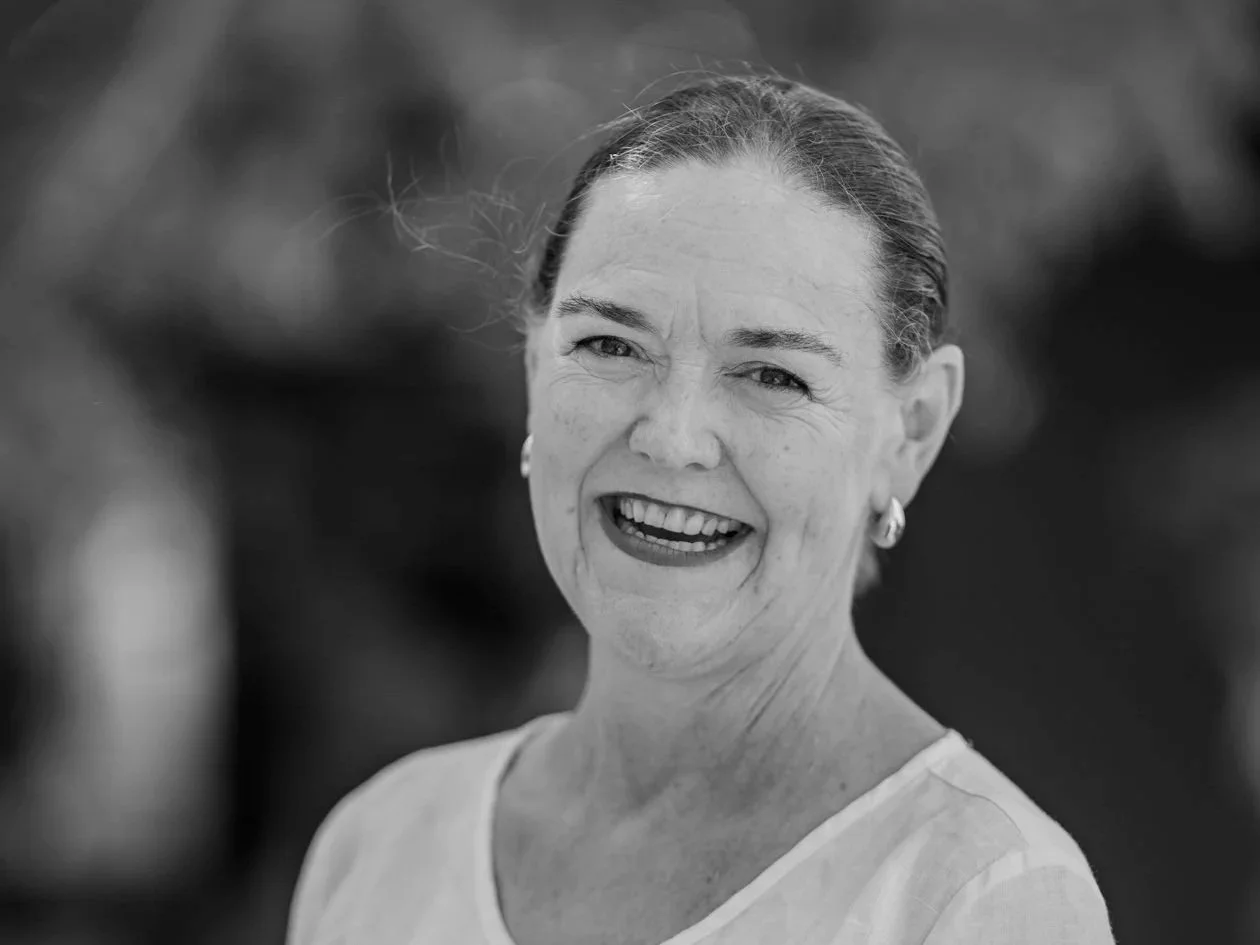 Black and white photo of dark haired woman smiling at camera wearing white v-neck top