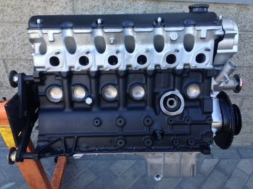 A car engine with a black and silver color scheme, mounted on a wooden stand outside against a brick wall.