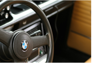 Close-up of a black steering wheel with the BMW logo, inside a vehicle with brown seats.