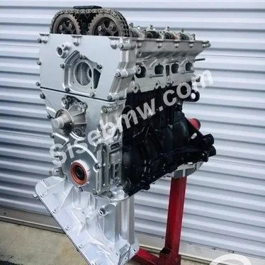 Automobile engine mounted on a stand in front of a metal wall.