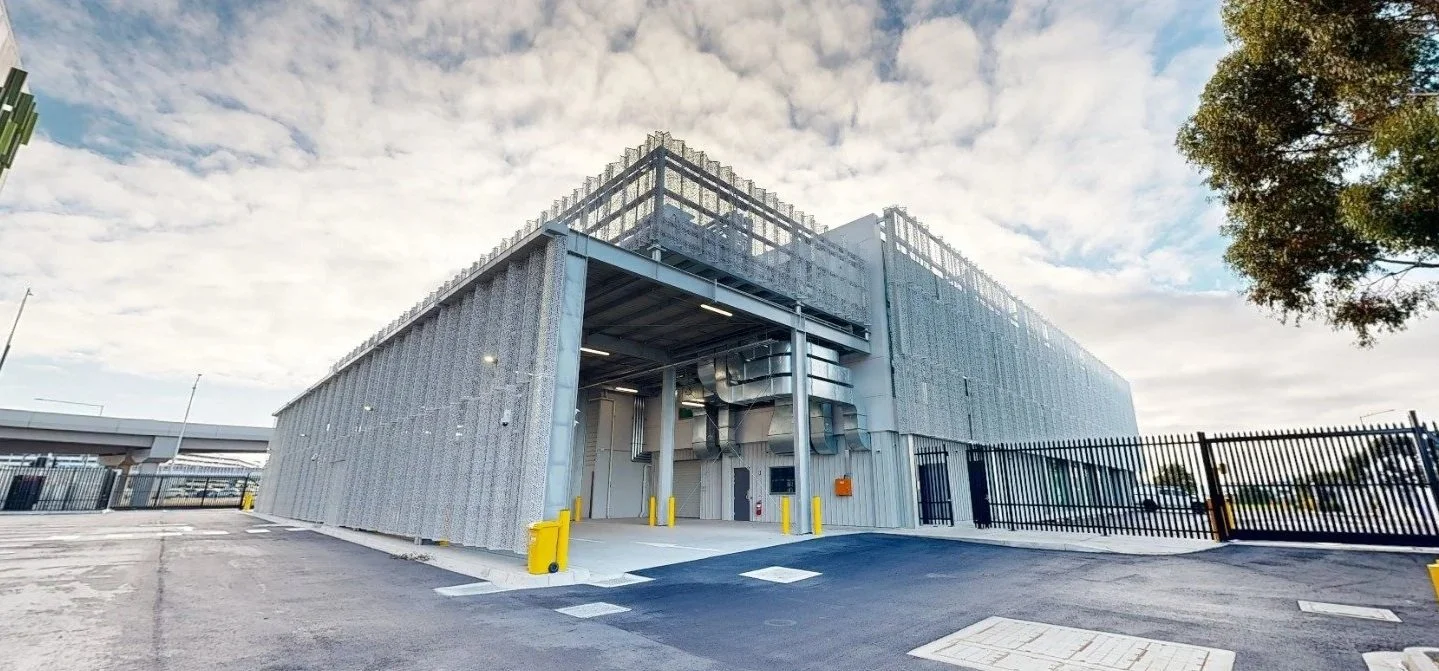 Exterior of a large industrial or commercial building with metal siding, ventilation ducts, and a gated entrance.