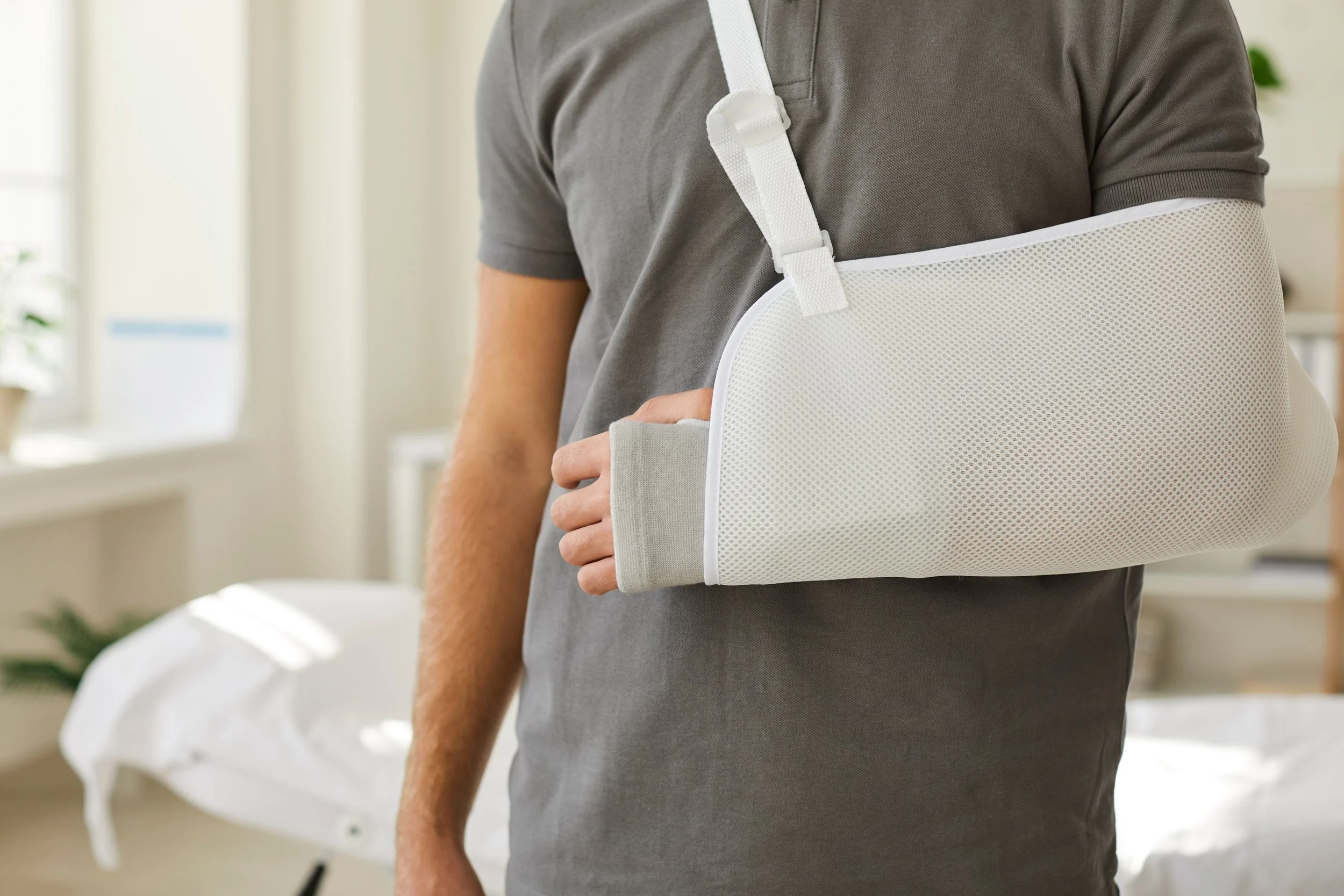 Person wearing a gray shirt with a white arm sling in a room with natural light.