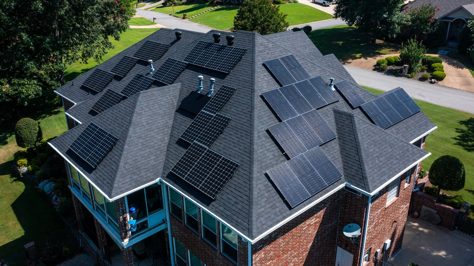 An aerial view of a house rooftop with multiple solar panels installed on the dark gray shingled roof.