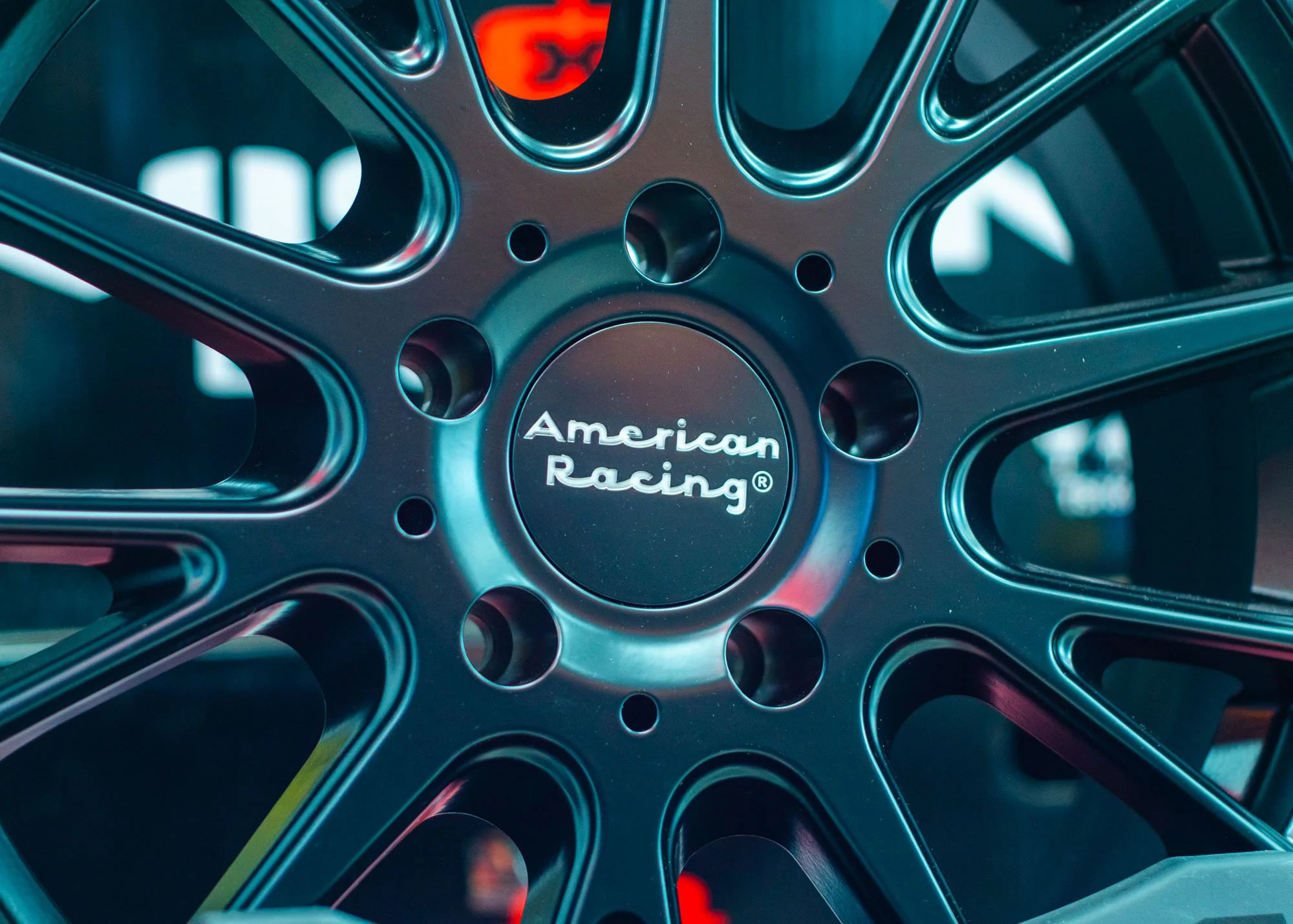 Close-up of a metallic racing wheel with the words American Racing engraved on it, showcasing a design with multiple holes and a shiny finish.
