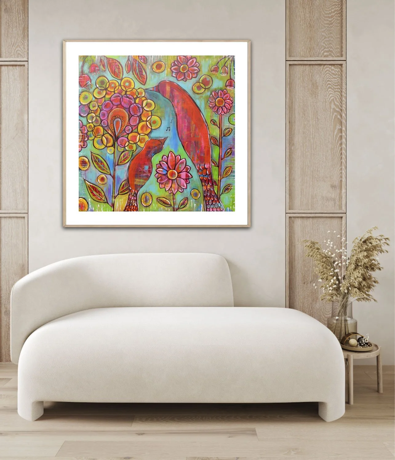 Colorful abstract painting of two pink and orange birds among flowers, hanging above a white curved sofa, in a modern living room with wooden panel accents and a small side table with a vase of dried flowers.