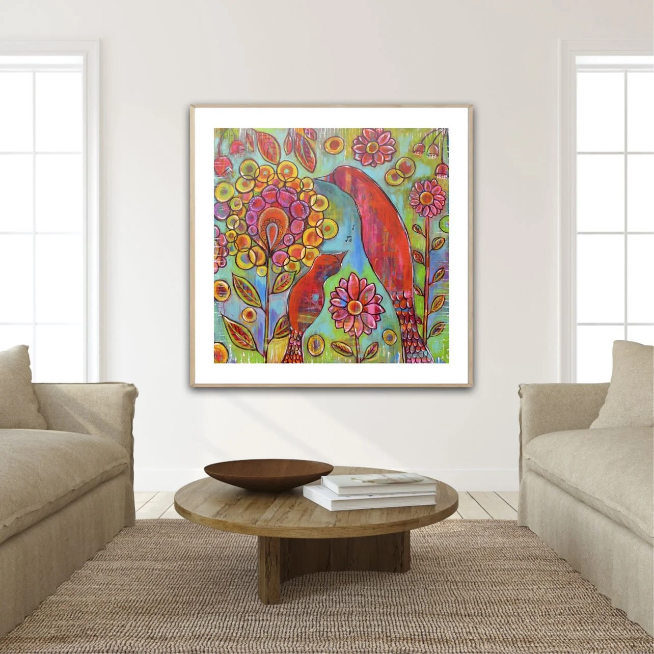 Colorful painting of two red birds among pink and orange flowers on a wall in a living room with beige sofas and a round wooden coffee table.