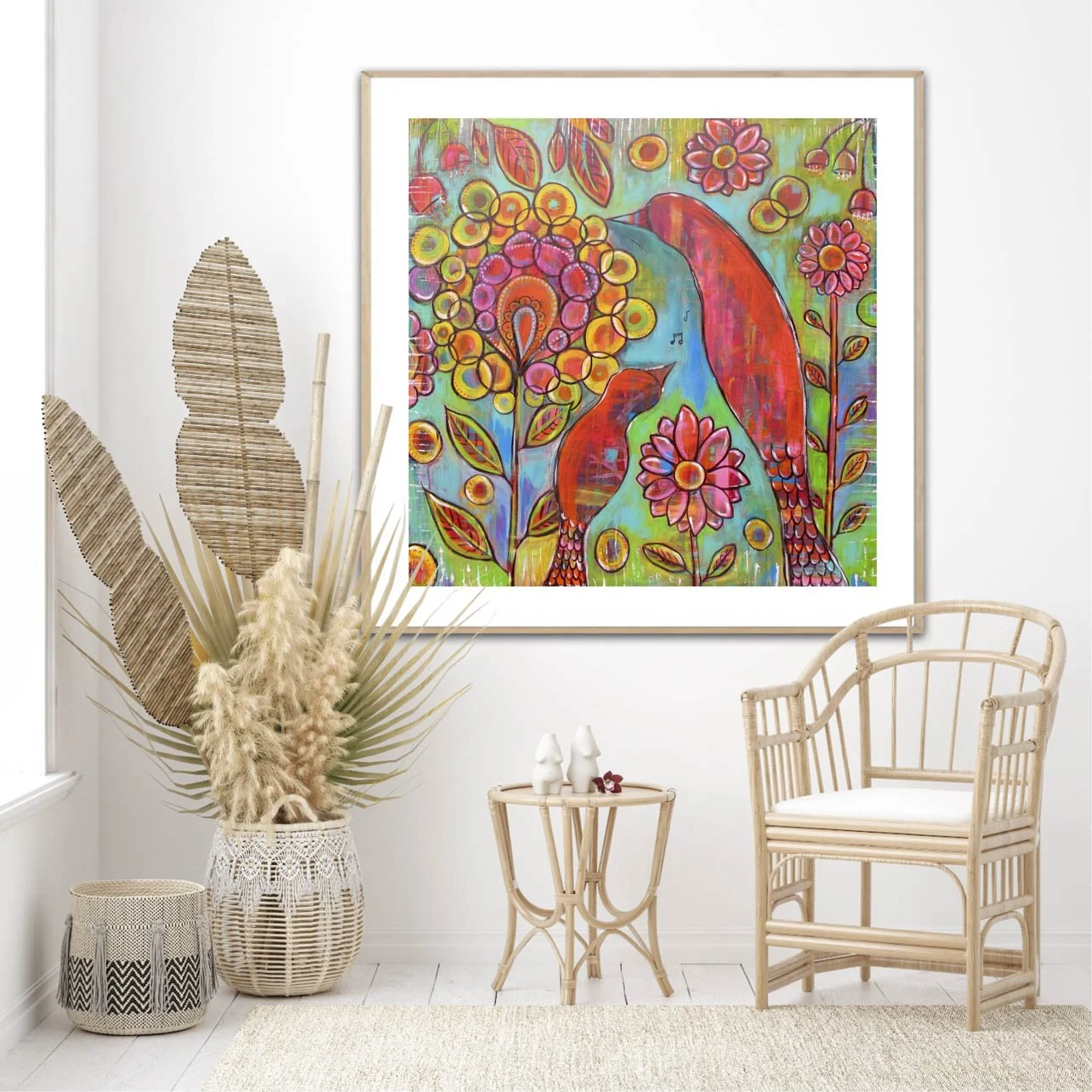 A bright, colorful abstract painting of birds among flowers hangs on a white wall in a cozy, boho-style room with wicker furniture and dried plants.