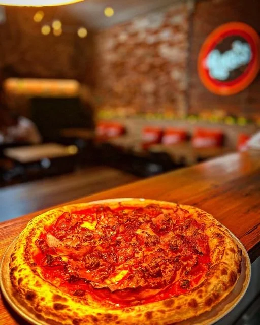 A pepperoni pizza on a wooden table in a cozy restaurant setting with exposed brick walls and dim lighting.