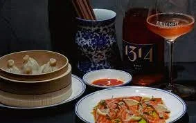 Various foods and beverages, including a bowl of dumplings, a bowl of dipping sauce, a plate of pizza, a blue patterned cup, a glass of rosé wine, and a wine bottle labeled 13.4.